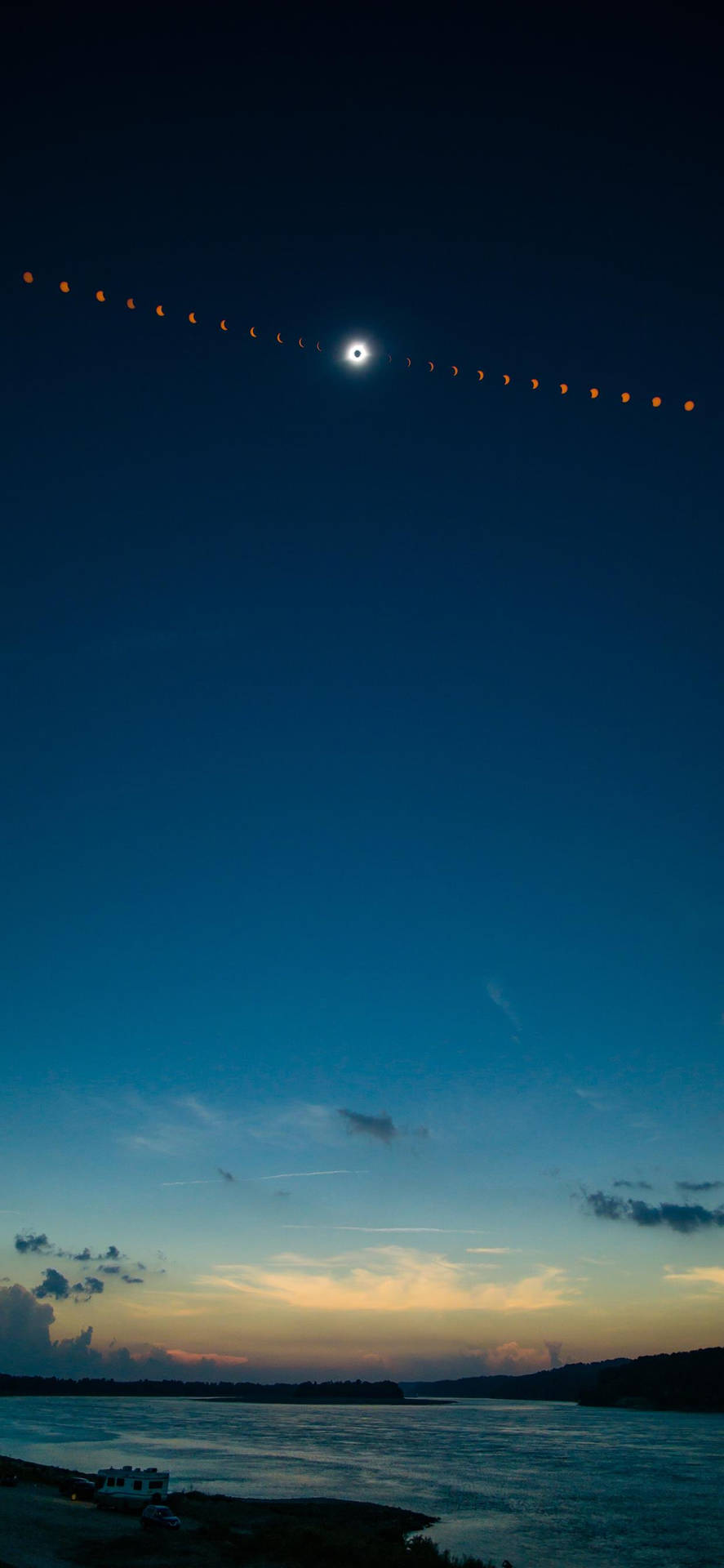 黃昏時河流上空的日食延時攝影，深藍色天空和橙色地平線。