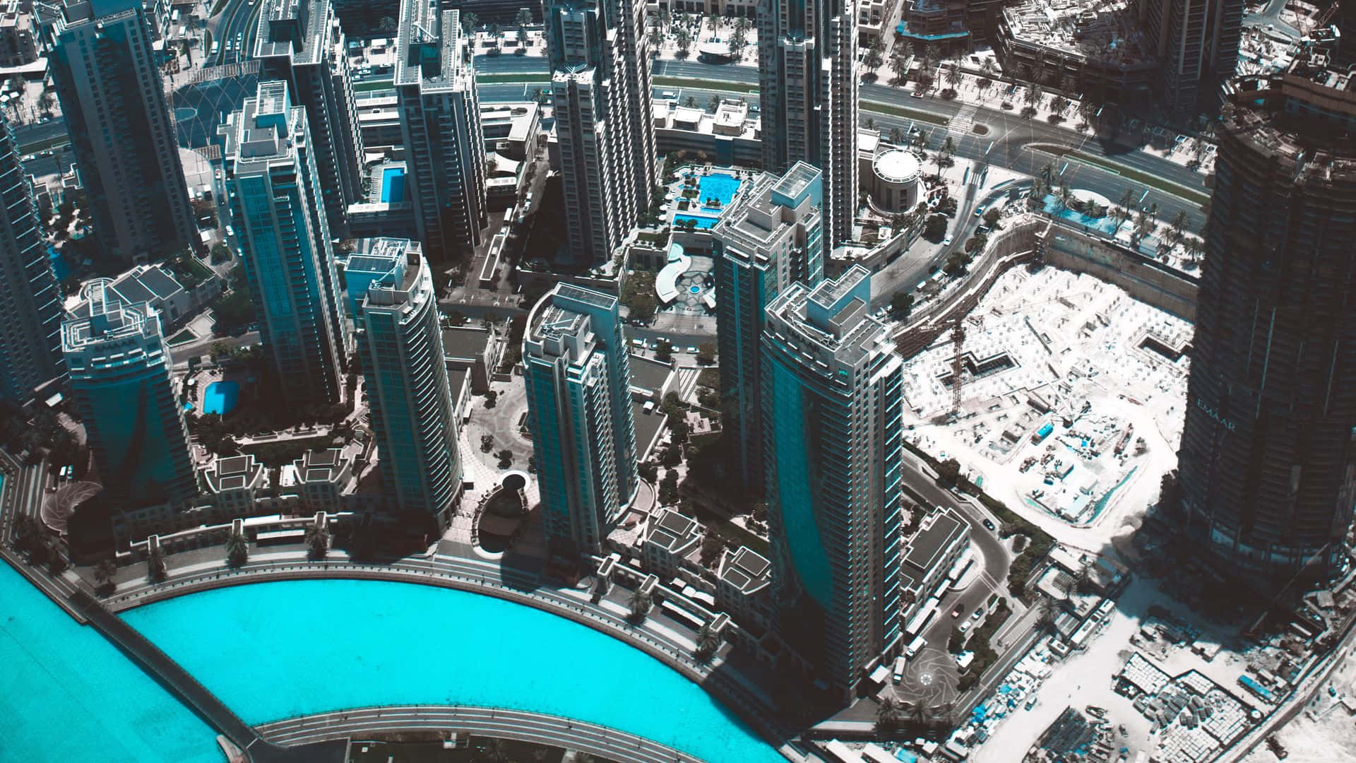 Burj Khalifa 桌布 壁紙 — 密集城市中心嘅未來主義摩天大樓圍繞住一個明亮嘅綠松石色人工湖嘅航拍圖。