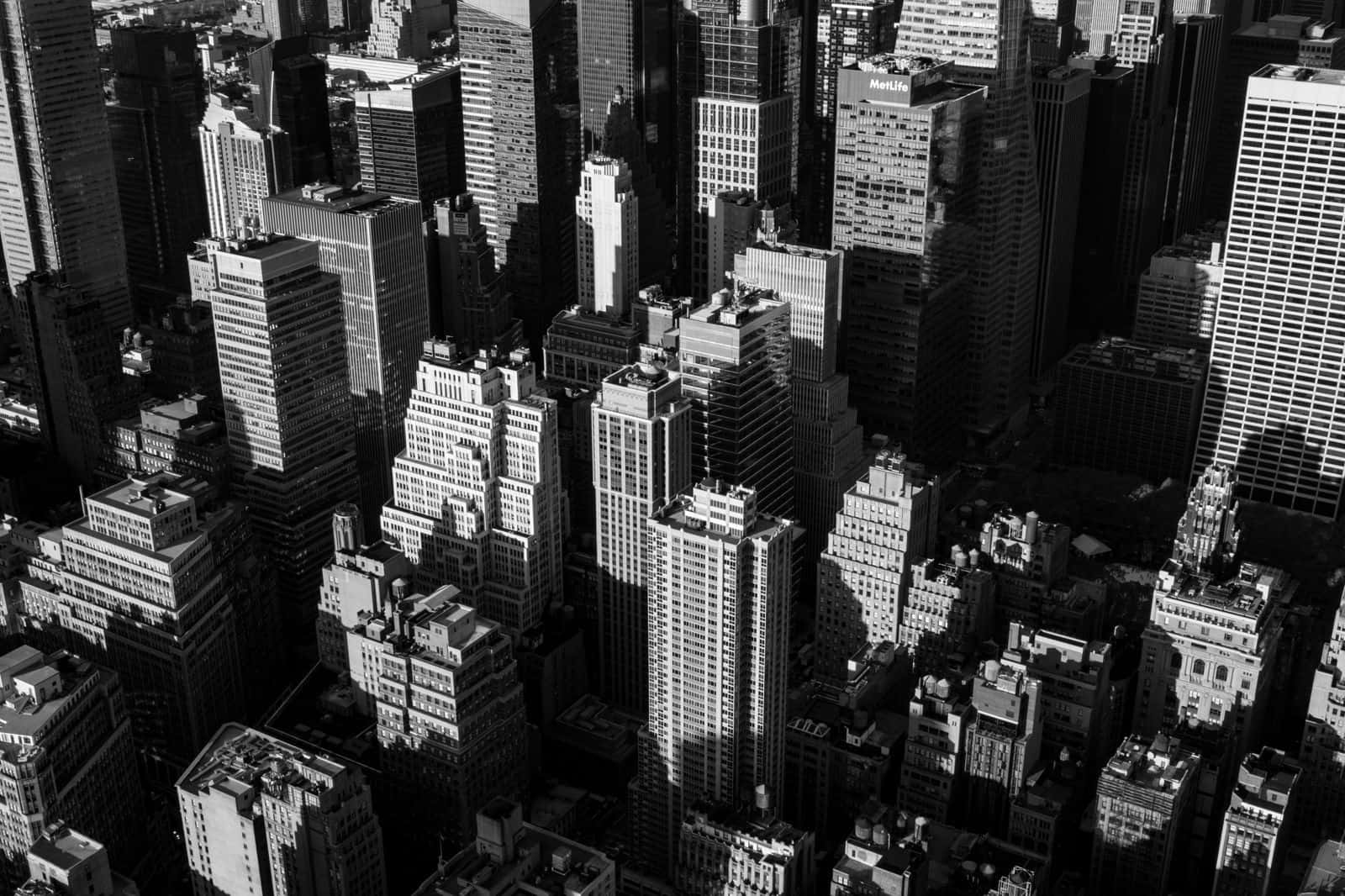 Black And White Cityscape 桌布 壁紙 — 密集城市峽谷中高聳摩天大樓投射出銳利陰影的黑白航拍視圖。