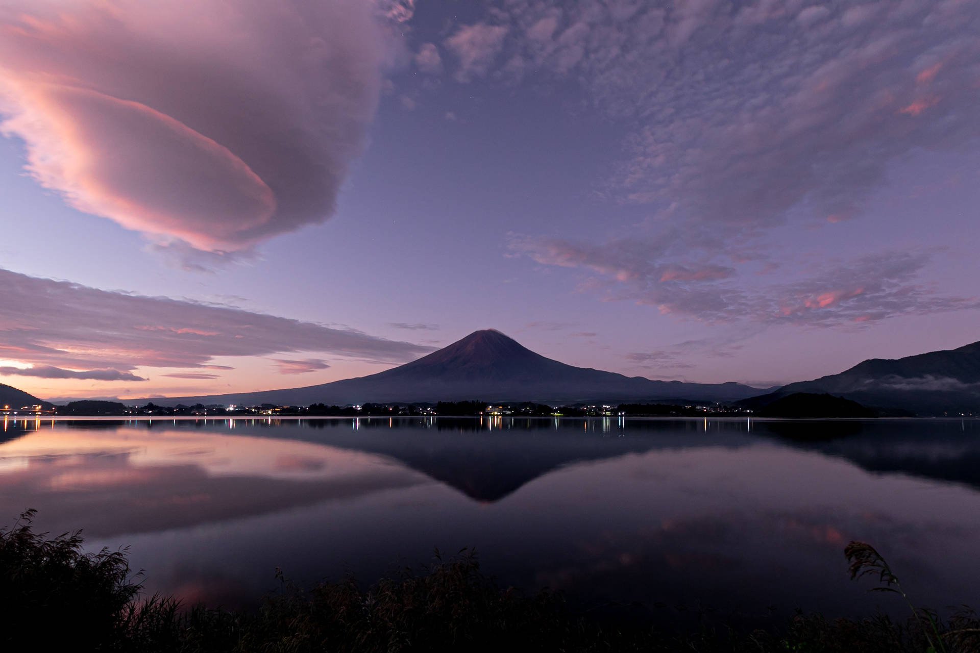 富士山在暮色中倒映在湖中，帶有粉紅色和紫色的雲彩。