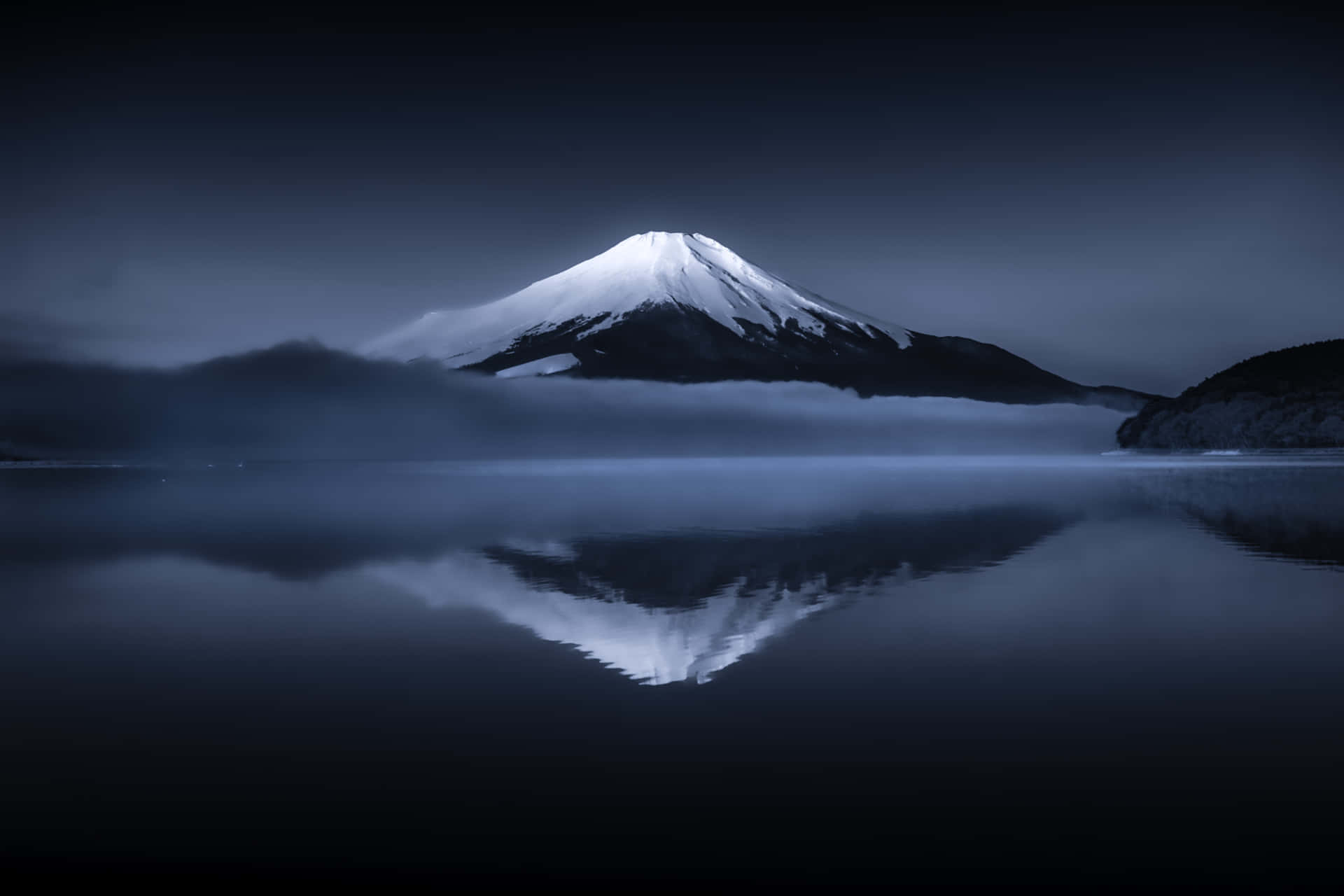 富士山在平靜的水面上倒映，天空陰暗有霧。