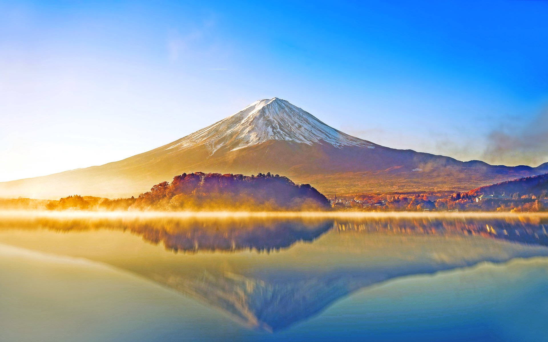 富士山倒映在霧氣繚繞的湖面上，日出時分，秋樹環繞