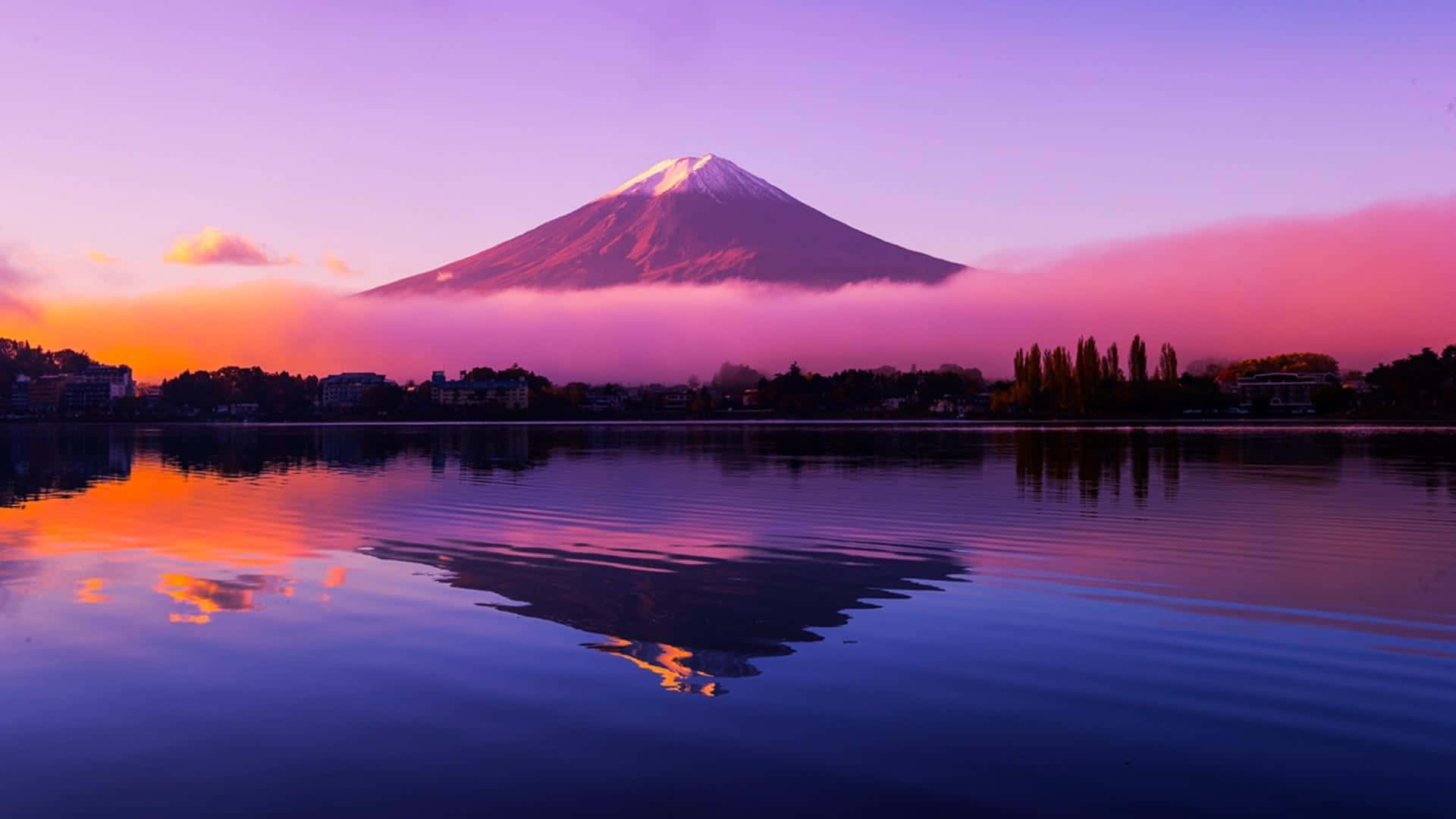 富士山周圍濃霧 壁紙 — 被雪覆蓋的富士山在黎明時分從霧氣中升起，其倒影在粉紫色天空下的平靜水面上閃爍。