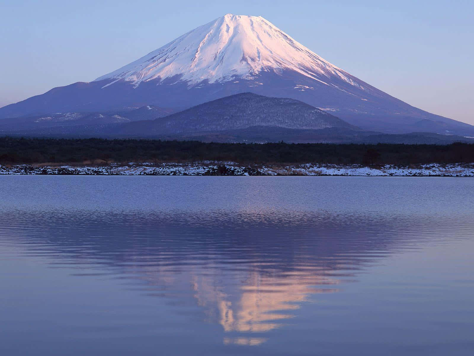 富士山日落的壯麗景色 壁紙 — 白雪覆蓋的富士山在黎明時分平靜地倒映在寧靜的湖面上，帶有柔和的紫色和藍色色調。