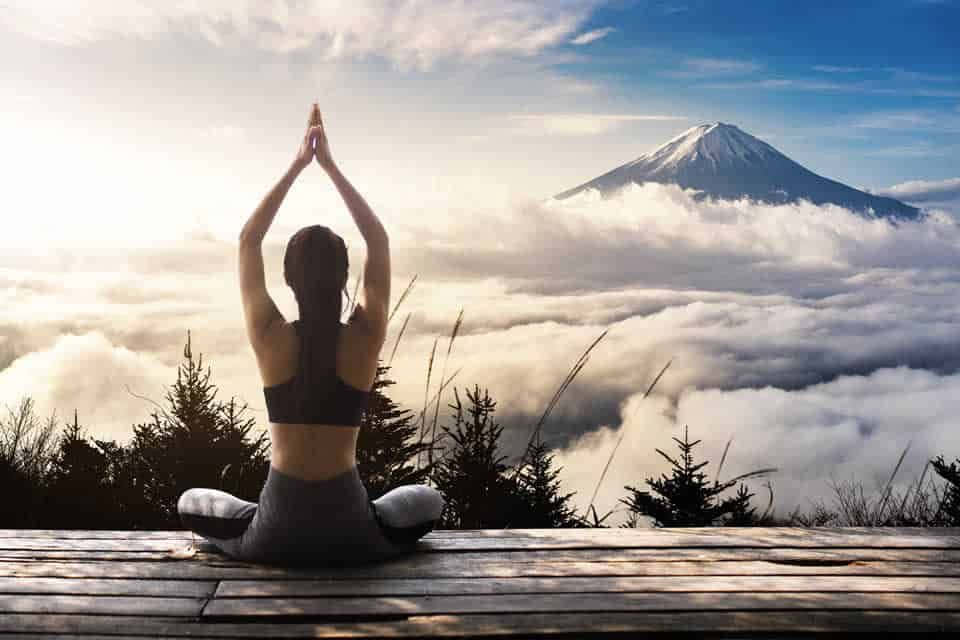 人在木製平台上以瑜伽姿勢冥想，下方有富士山和雲海。