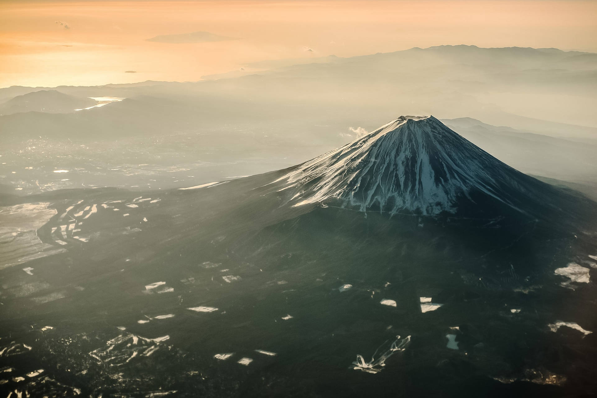 白雪覆蓋的富士山沐浴在金色的日出光芒中，下方是霧氣繚繞的山谷。