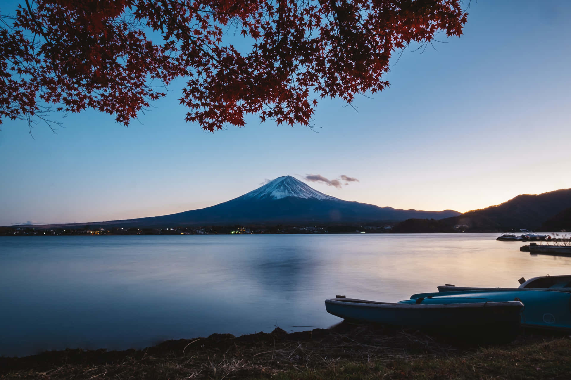 富士山與湖景 壁紙 — 深紅的楓葉框住寧靜的暮色景色，積雪的富士山倒映在平靜的水面上，附近停泊著船隻。