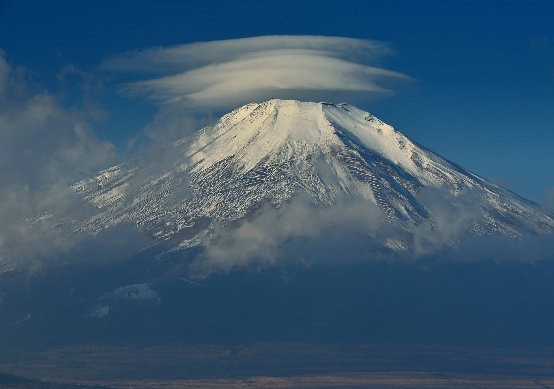 白雪覆蓋的富士山，山頂上方有透鏡狀雲，背景是清澈的藍天。