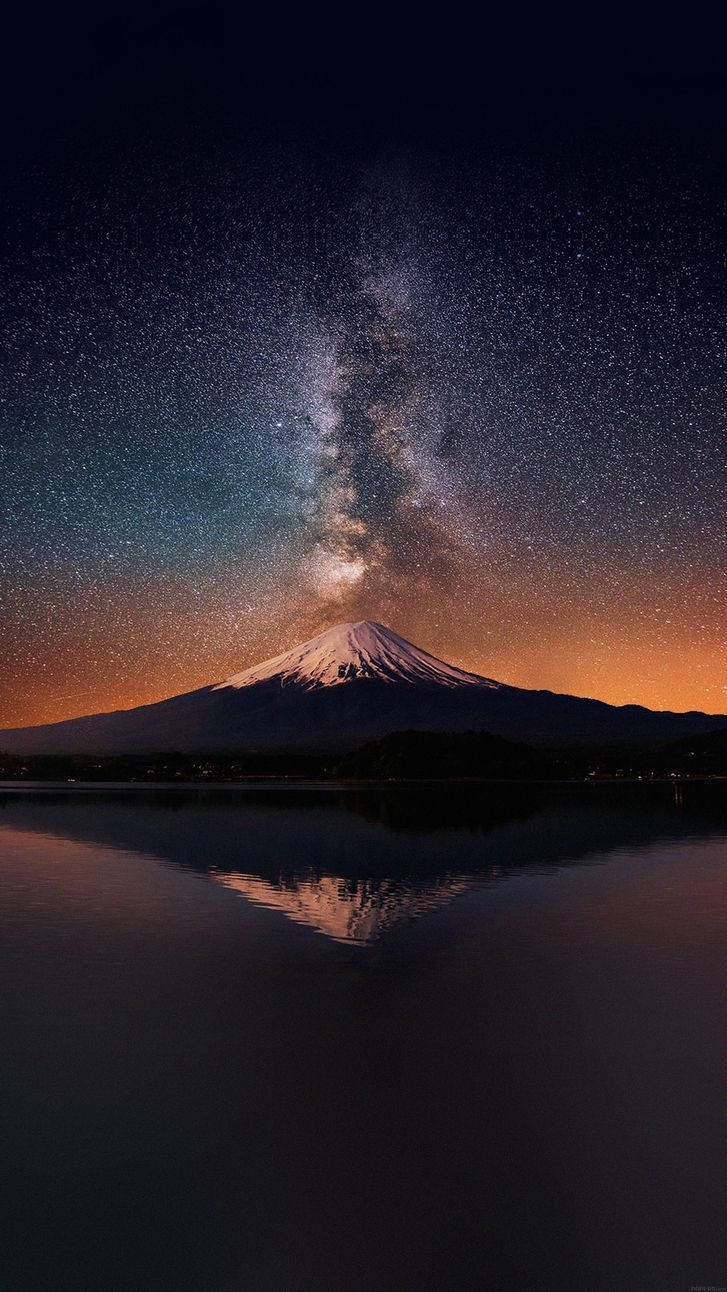 富士山頂部 iPhone 壁紙 — 白雪覆蓋的富士山在平靜的水面上完美倒映，上方是燦爛星空，銀河拱橋般橫跨天際。