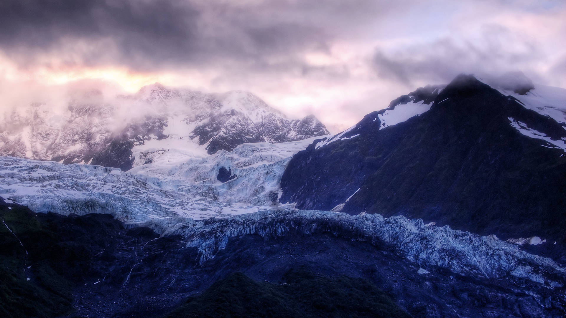 寒冰山景 壁紙 — 壯麗的冰川流經積雪覆蓋的山脈，在戲劇性的暮色天空下，帶有粉紅色和紫色的雲彩。