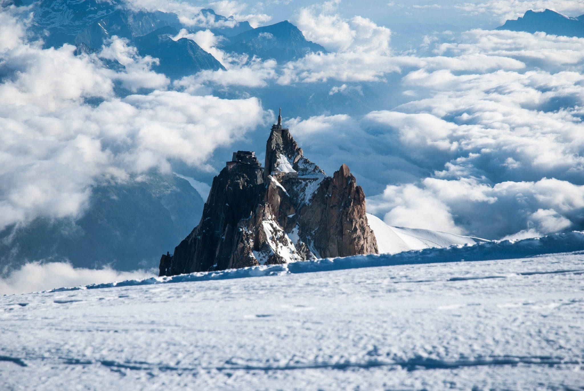 寒峰之境 壁紙 — 白雪覆蓋的山峰戲劇性地聳立在雲海之上，一座歷史悠久的城堡棲息在其岩石頂峰。