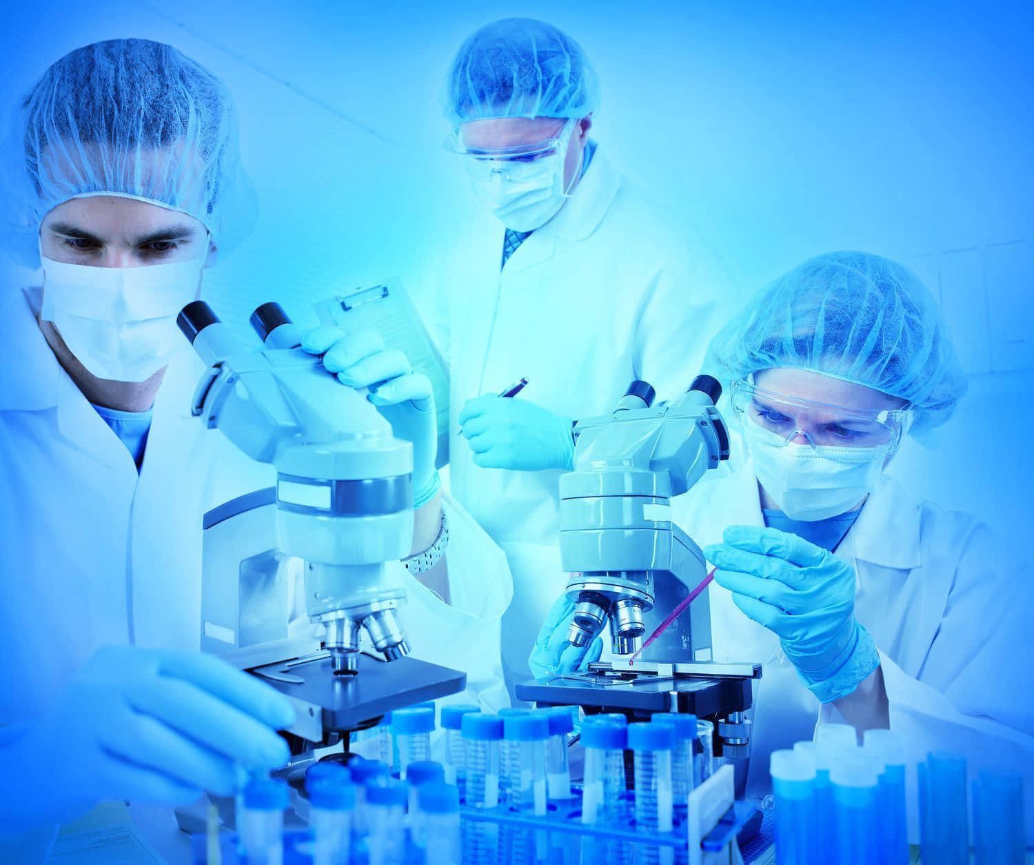 三位身穿實驗室外套和口罩的科學家使用顯微鏡和試管。