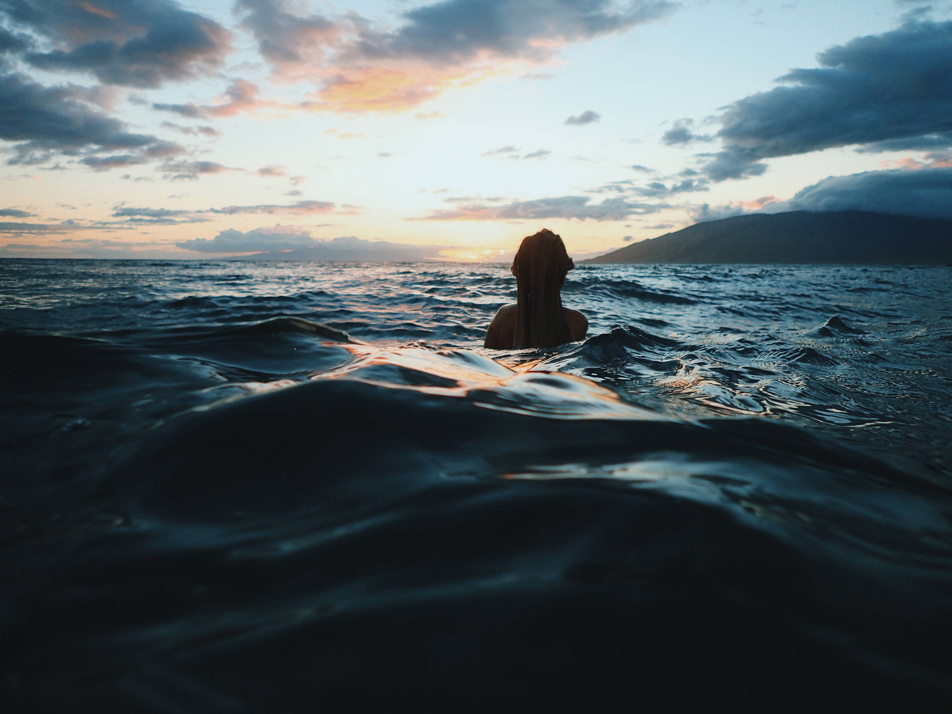 夕陽下在海中漂浮的人，背景有山