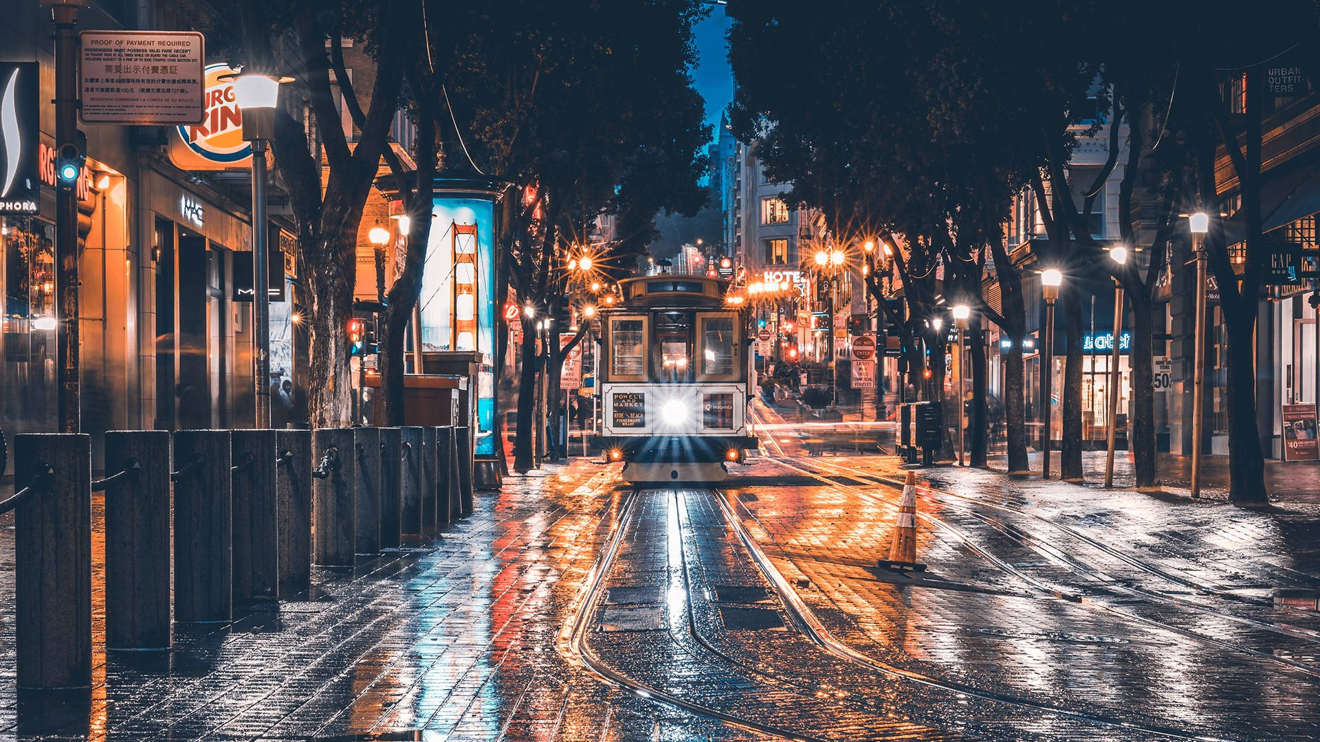 寧靜優雅的街道風景 壁紙 — 一輛纜車在夜間沿著濕漉漉的三藩市街道滑行，車頭燈穿透濕滑的路面，閃爍的街燈在波光粼粼的水坑中反射。