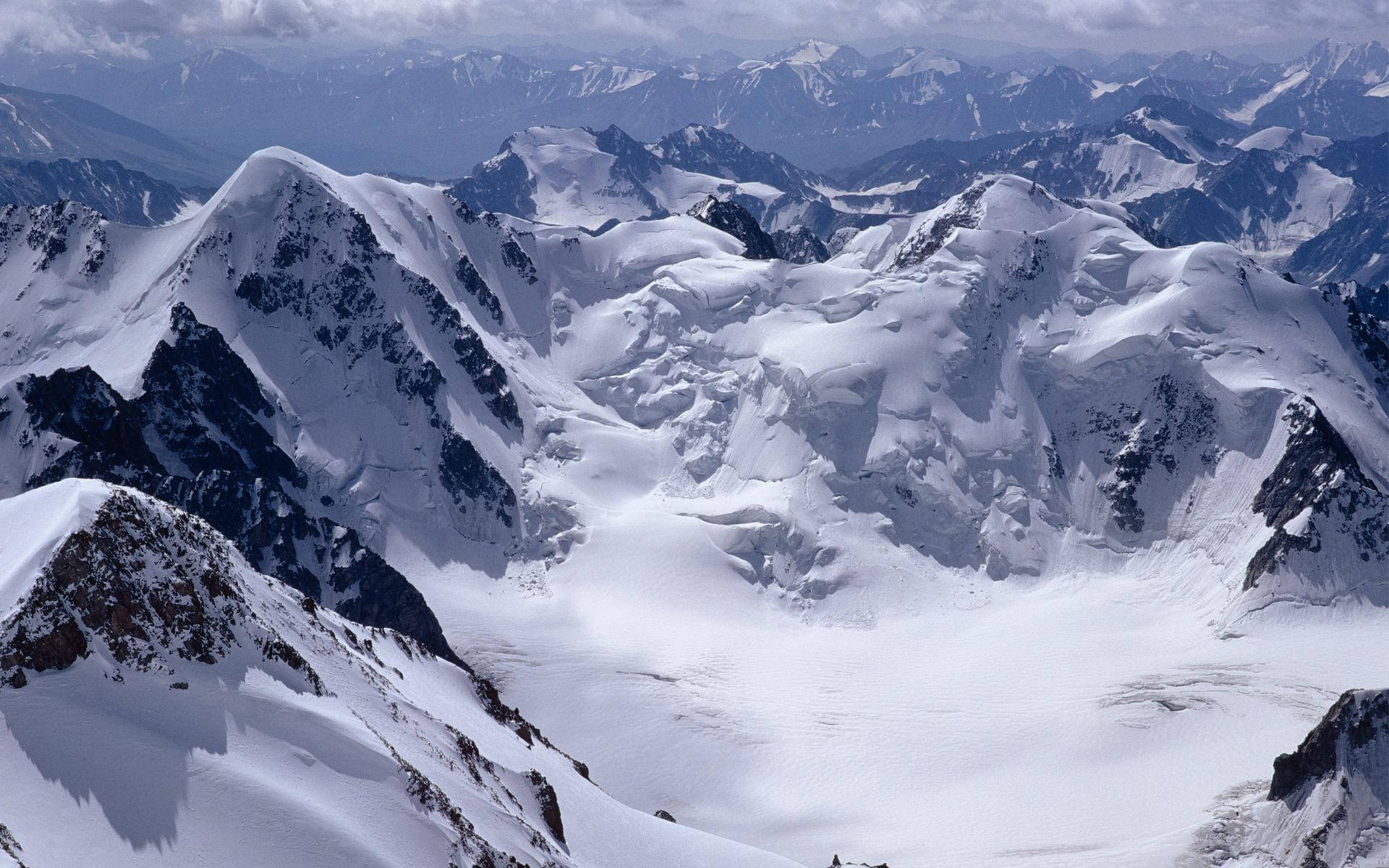 寧靜冬日仙境 壁紙 — 在陰天下一覽無遺的雪峰和冰川的航拍美景。