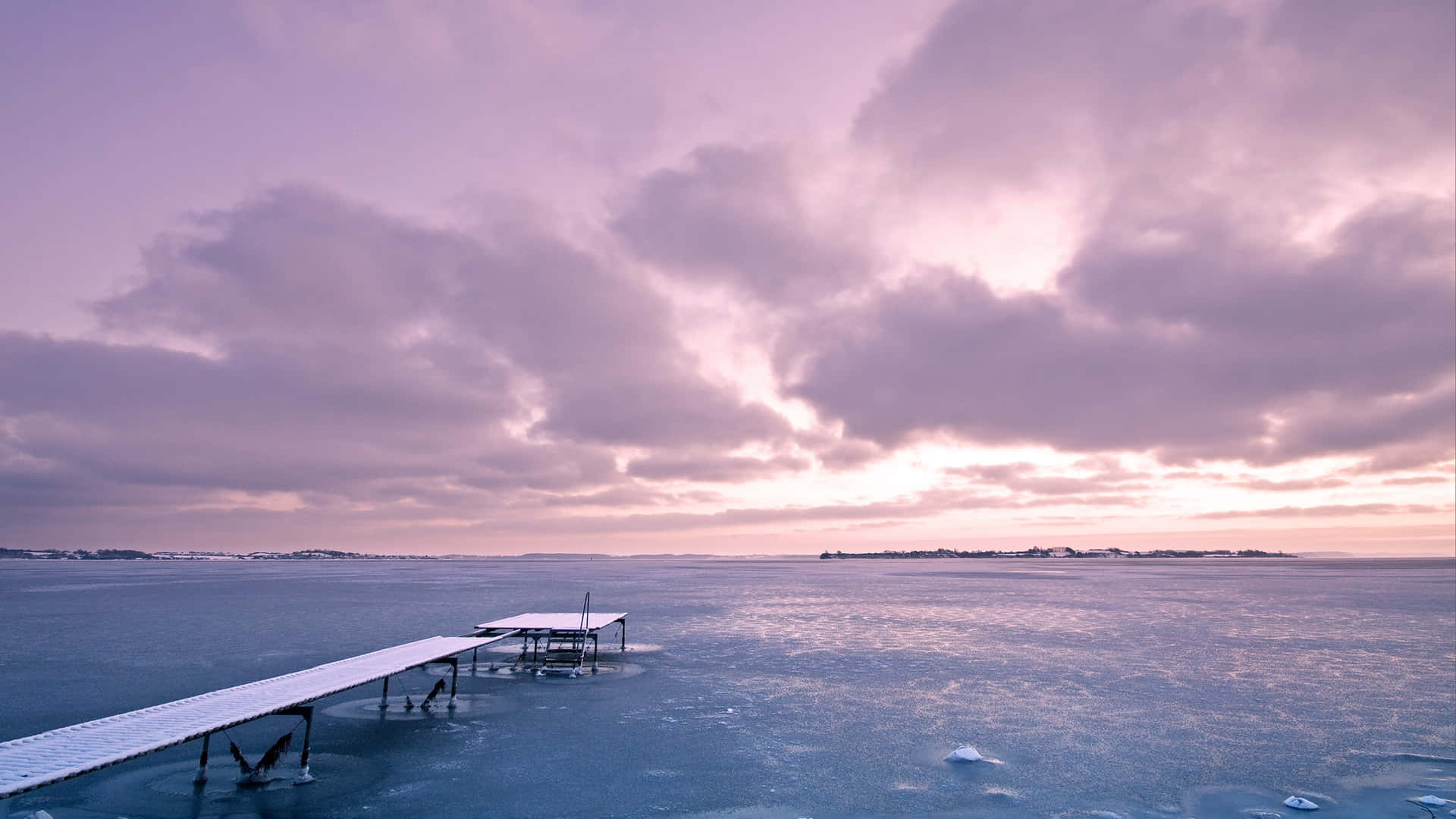 寧靜冰海風景 壁紙 — 一條灑滿雪的木碼頭延伸至冰封的湖面上，背景是戲劇性的紫色和粉紅色黃昏天空。