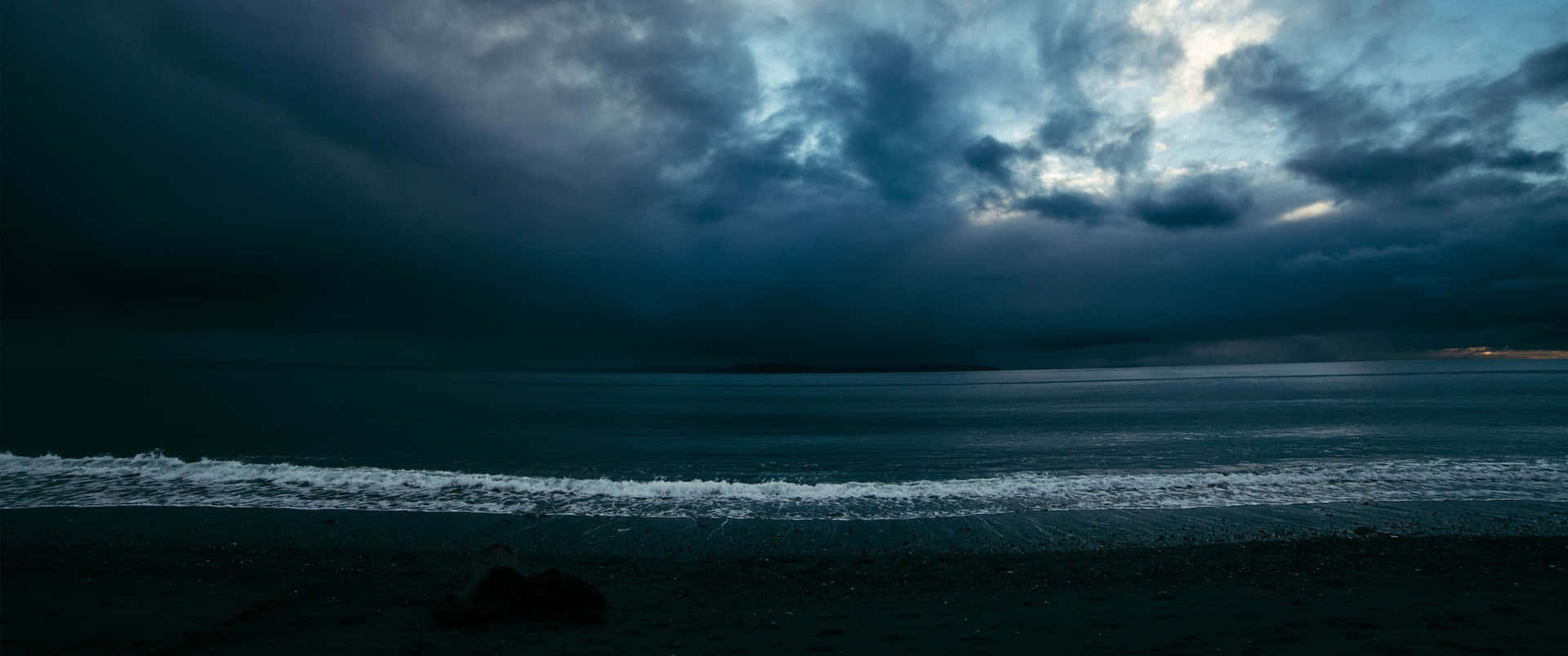 黑暗的海浪在黃昏時分厚重的雲層下拍打著暴風雨的海灘。