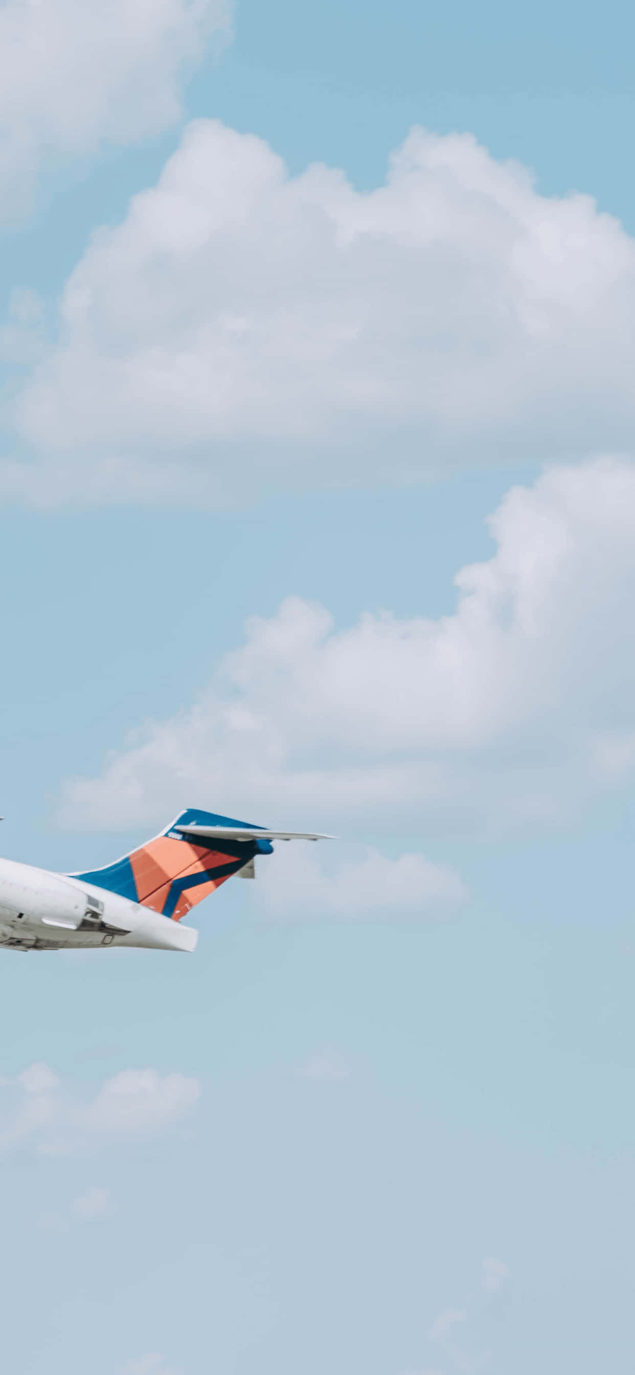 寧靜天空：寧靜平和淺藍背景 壁紙 — 近距離拍攝飛機尾部，藍橙配色在藍天白雲中翱翔。