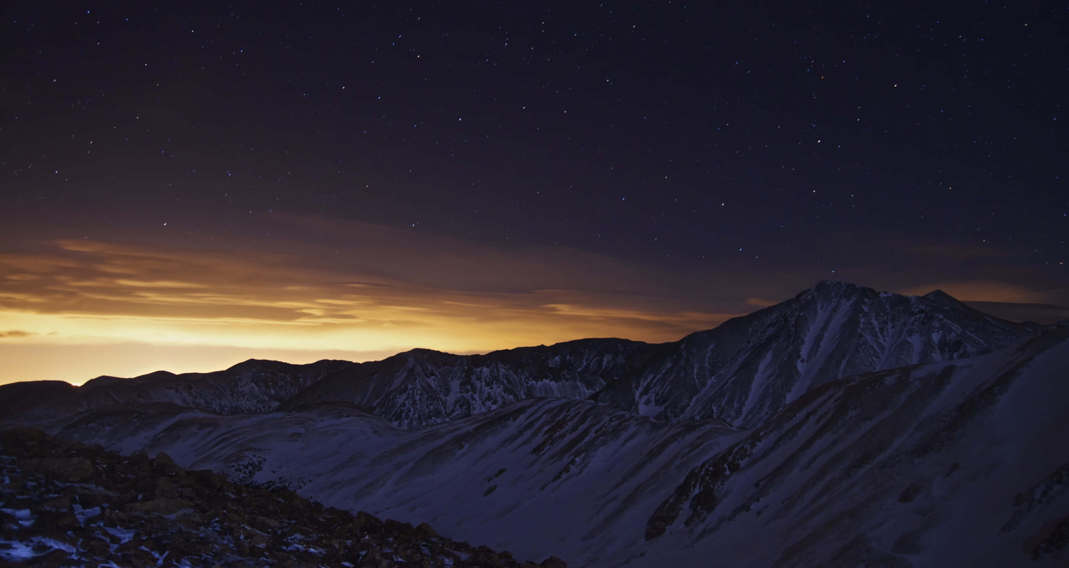 寧靜月光夜空 壁紙 — 白雪覆蓋的山峰在繁星點點的夜空下映襯著發光的橙色地平線形成剪影。