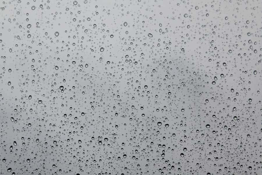 「寧靜水波中閃耀的碧綠色調」 壁紙 — 雨滴依附在玻璃表面，以柔和的灰色天空為背景，營造出柔和模糊的背景。
