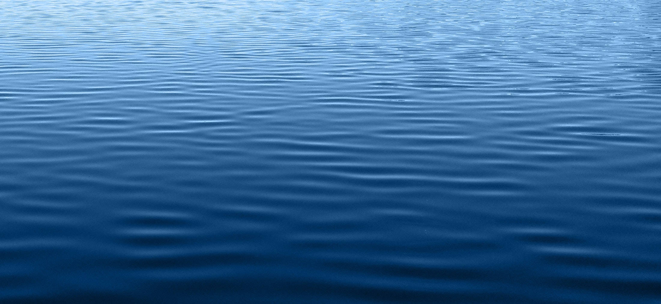 寧靜海景背景 壁紙 — 平靜深藍色水在柔和光線下輕輕泛起漣漪，營造出寧靜祥和的自然景象。