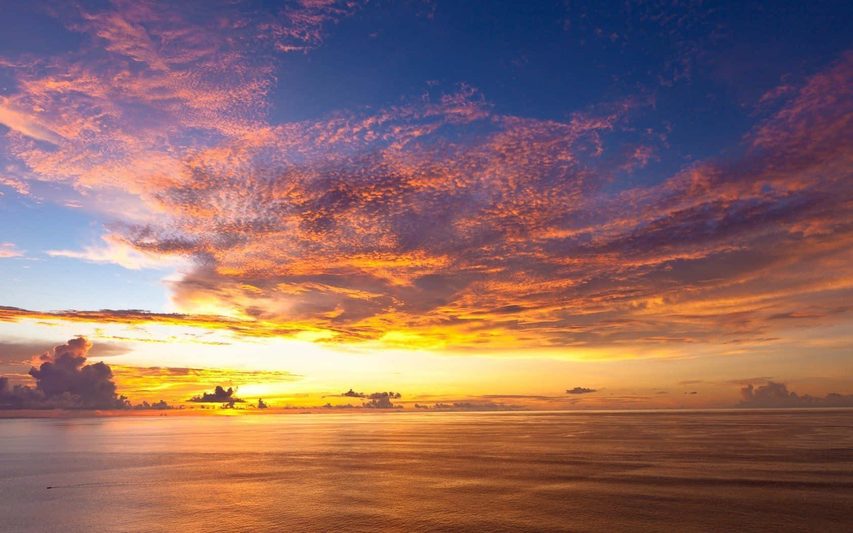 Yellow Sky 桌布 壁紙 — 寧靜海洋上令人驚嘆的日落，火熱的橙色和紫色雲彩倒映在水面上。