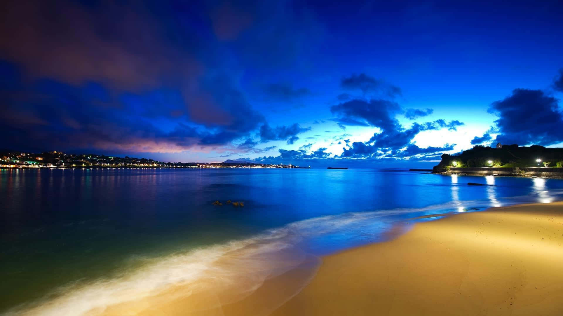 寧靜海灘桌面背景 壁紙 — 黃昏時分寧靜的海灘，金色沙灘在戲劇性的多雲天空下與平靜的藍色海水相接。