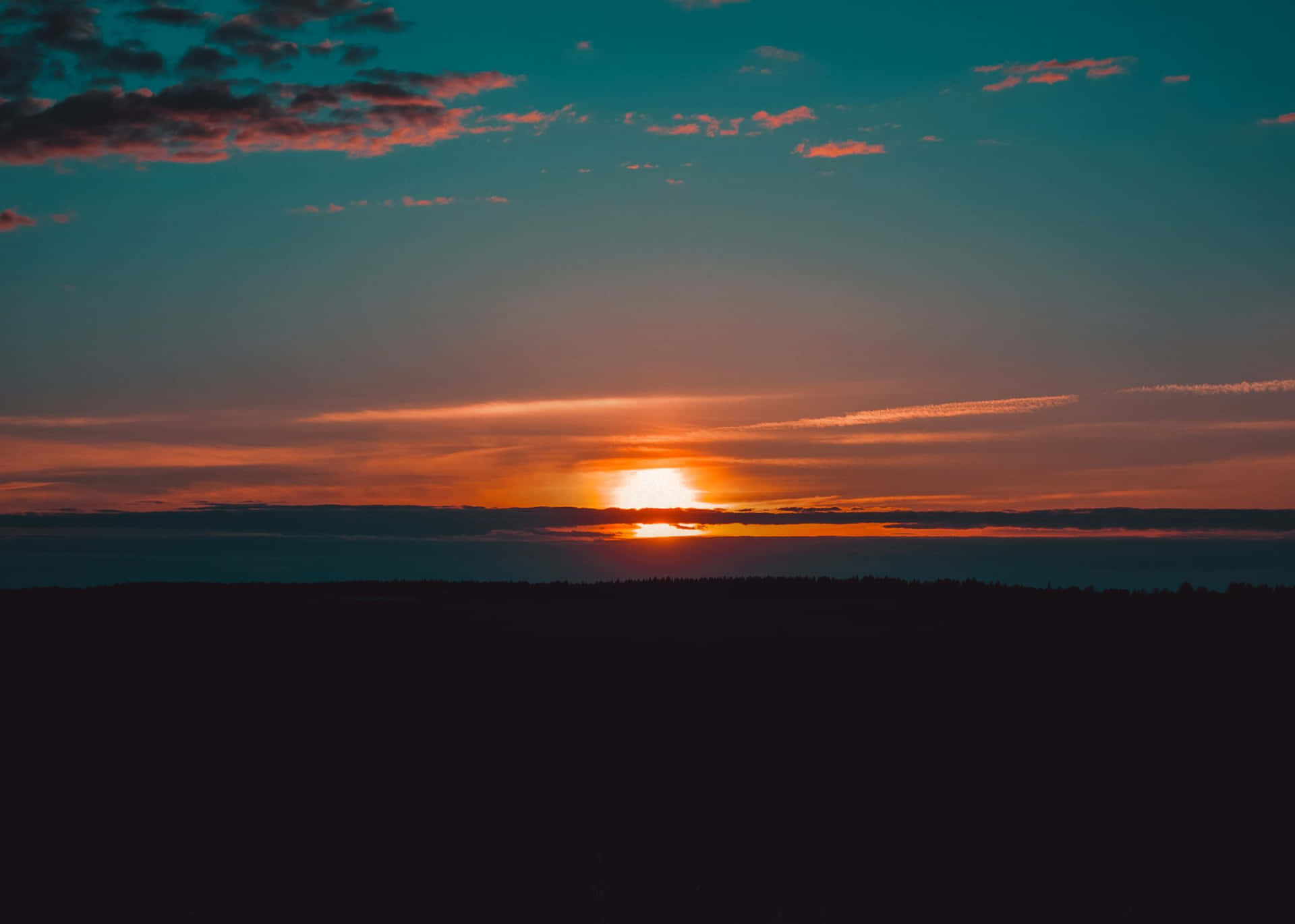 森林上空的夕陽，天空呈現橙色和藍綠色