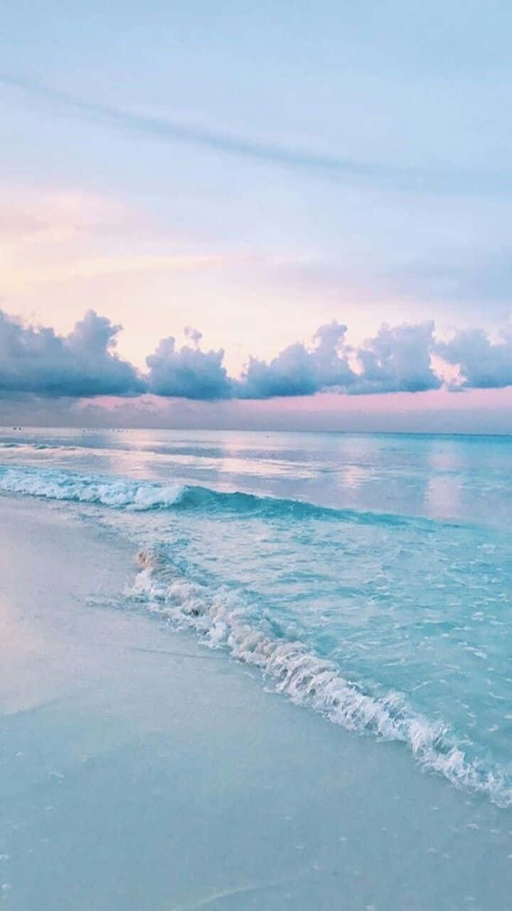 寧靜海灘美學手機壁紙 壁紙 — 柔和的粉彩波浪輕輕拍打寧靜的沙灘，天空夢幻的暮色中點綴著粉紅和藍色的雲彩。