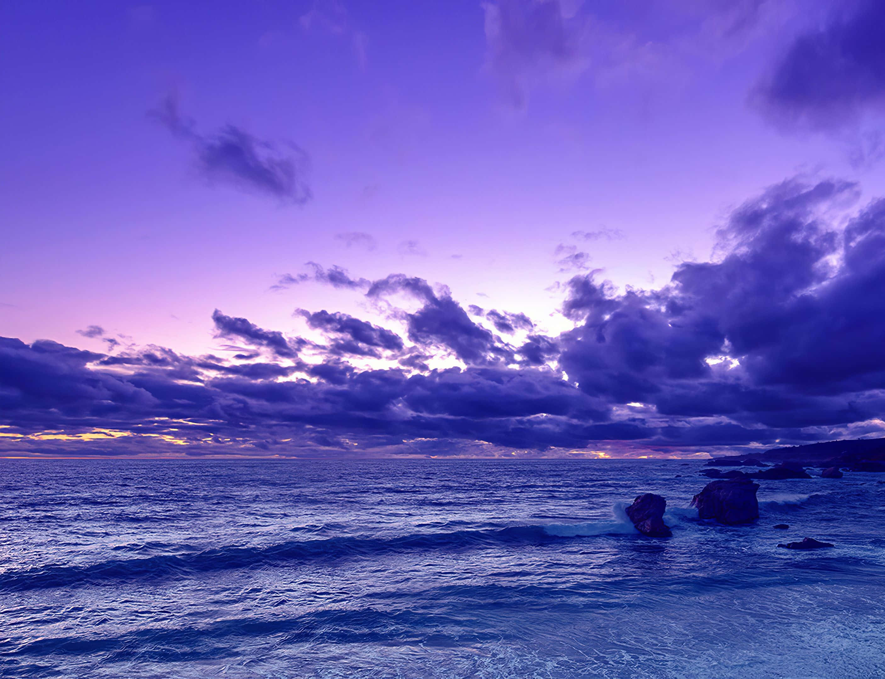 寧靜海面的日落美景 壁紙 — 在波濤洶湧的海洋上，紫色日落與烏雲和岩石海岸形成戲劇性景象。