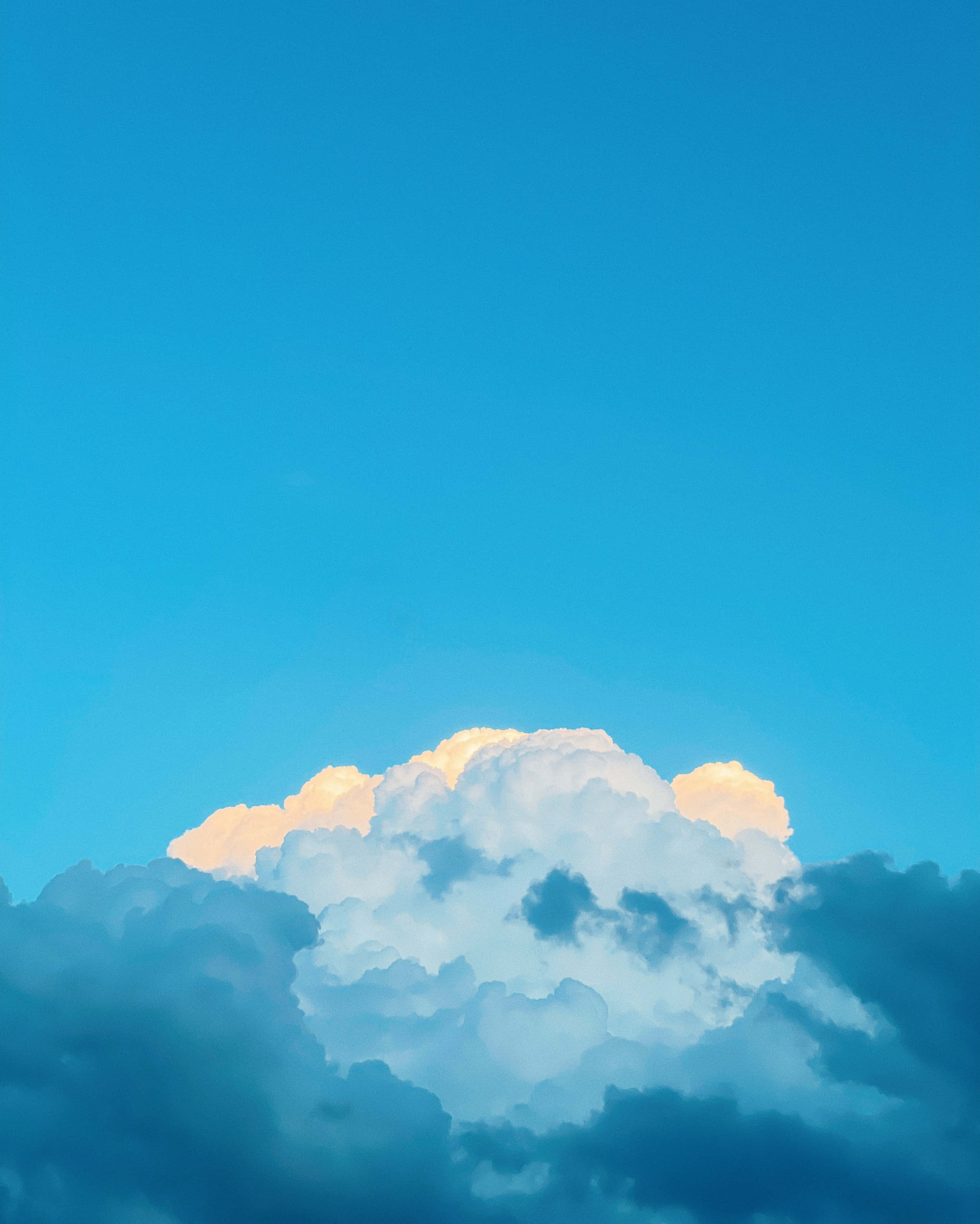 寧靜淡藍背景 壁紙 — 戲劇性的天空，頂部有蓬鬆的白雲在鮮豔的藍色背景下閃耀著金色光芒。