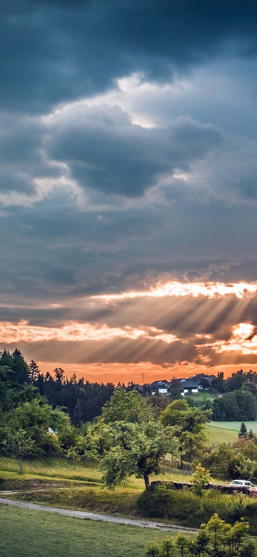 陽光穿過暴風雲，照耀在一個有樹木和房屋的綠色山谷上。