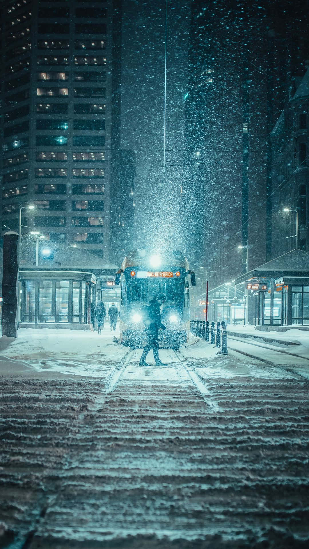 夜間城市街道上有人在雪中行走，巴士駛近。