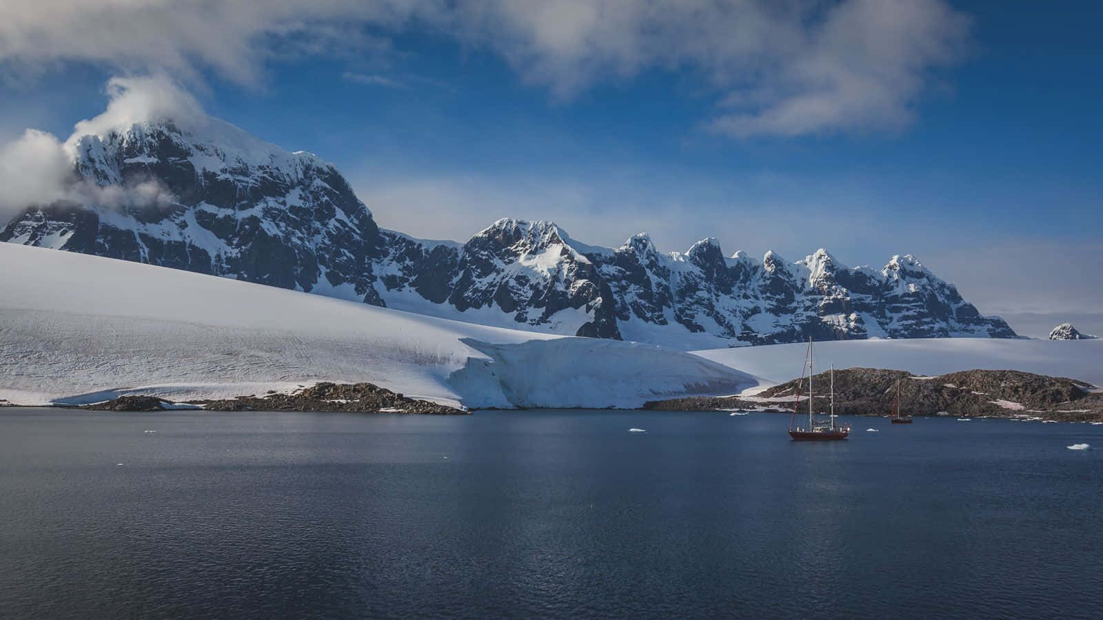 Antarctica 桌布 壁紙 — 寧靜的南極海灣，積雪覆蓋的鋸齒狀山脈倒映在平靜的水面上，兩艘帆船悠然漂浮。