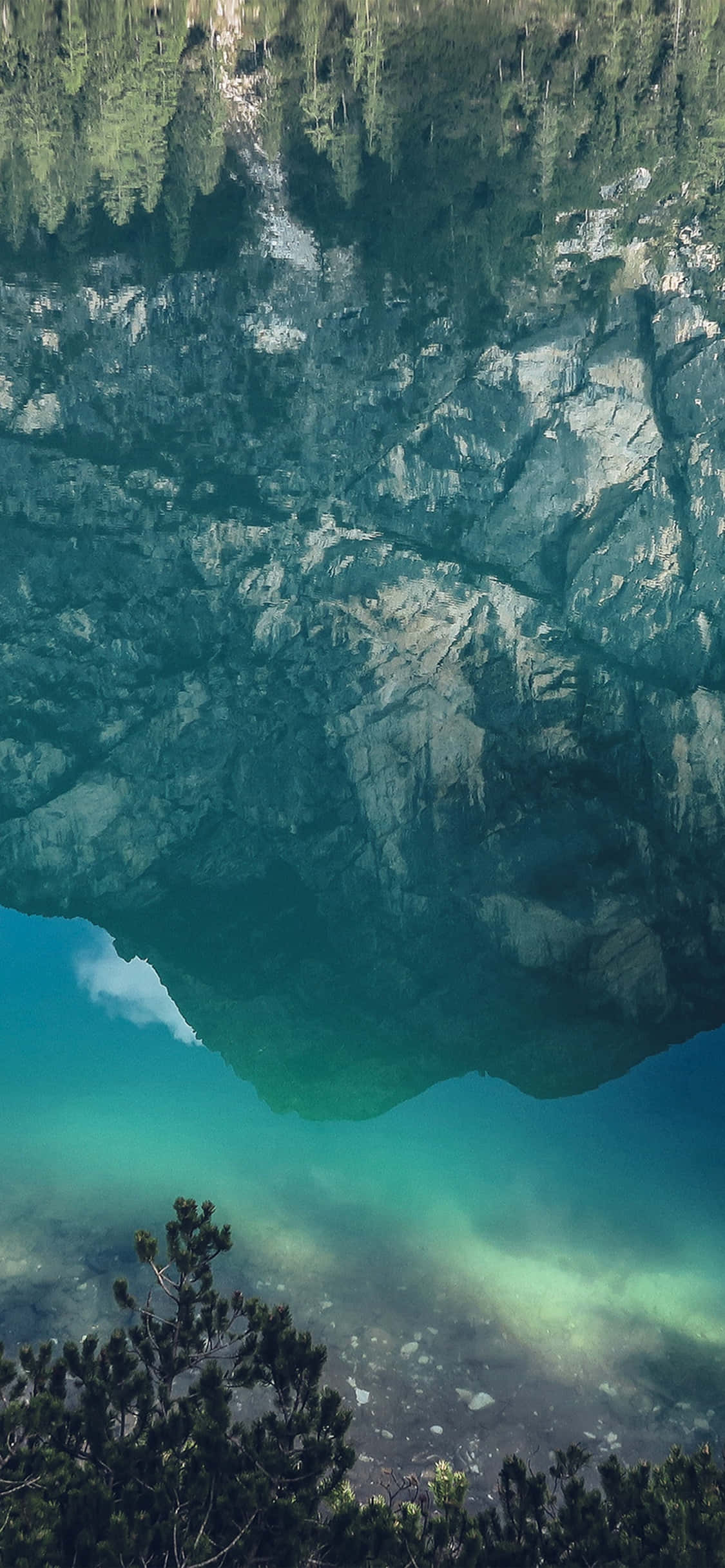 iPhone X Nature 桌布 壁紙 — 寧靜的山間湖泊映照著崎嶇的懸崖和松樹，湖水清澈見底，呈現藍綠色。