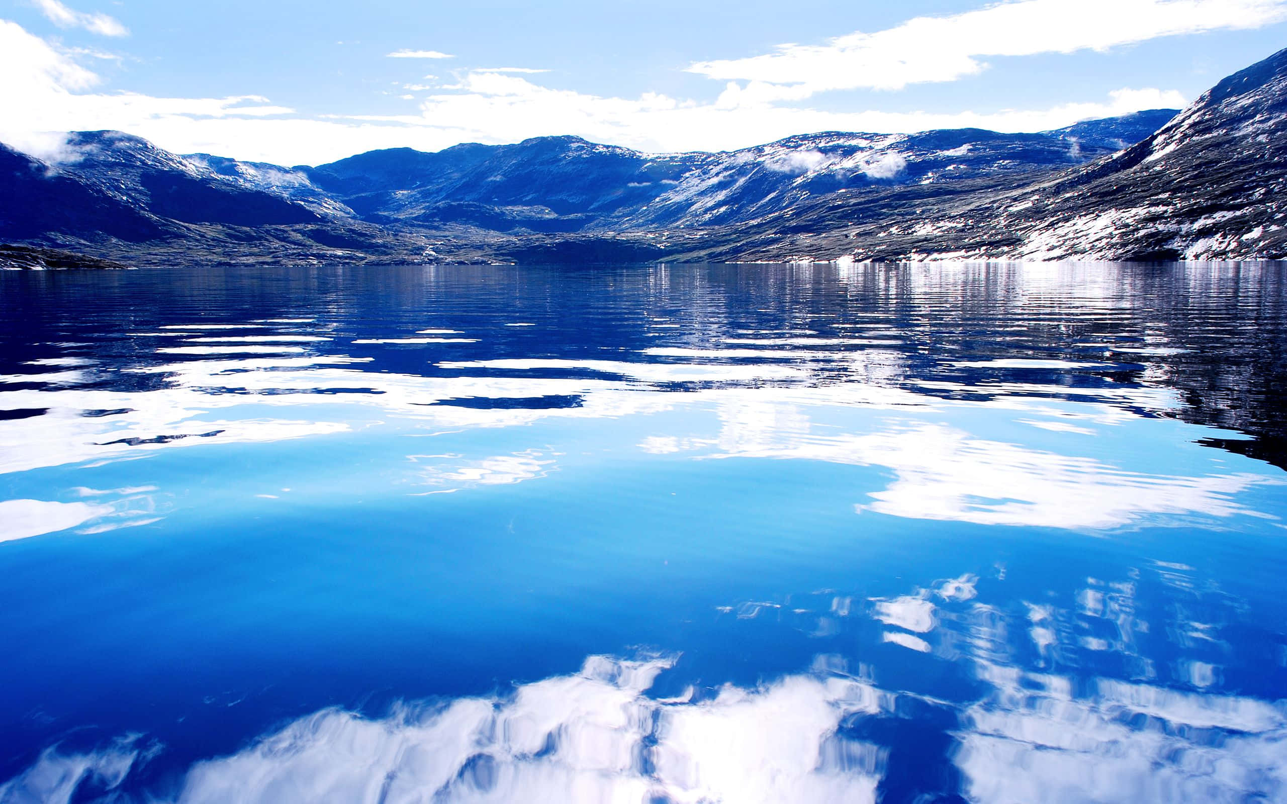 Greenland 桌布 壁紙 — 寧靜的山間湖泊映照著白雪覆蓋的山峰和藍天，在明亮的日光下。