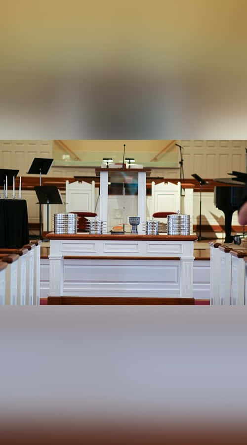 Sacrament 桌布 壁紙 — 寧靜的教堂內部，白色長椅和木製祭壇上放有疊起的銀盤和聖杯，在溫暖燈光下。