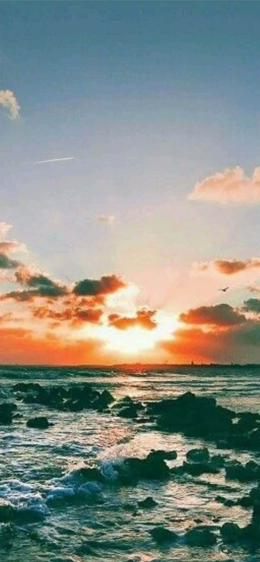 夕陽映照岩石海洋，色彩斑斕的雲朵和拍岸的浪花。