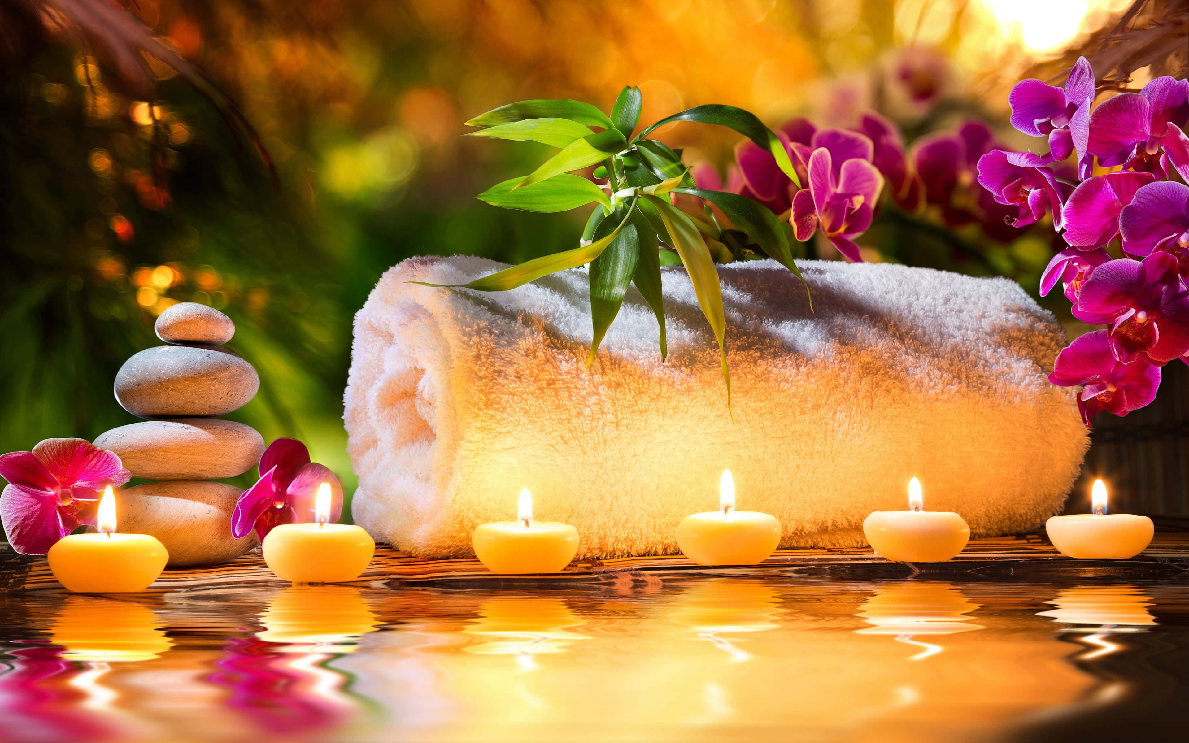Aromatherapy 桌布 壁紙 — 寧靜的水療場景，點燃的蠟燭在水面上反射，旁邊有捲起的毛巾、蘭花和堆疊的石頭。