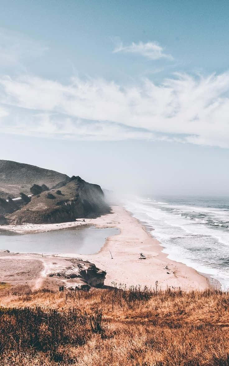 Winter Beach 桌布 壁紙 — 寧靜的海岸景色，沙灘沿著懸崖蜿蜒，天空柔和藍色，飄著縷縷白雲。