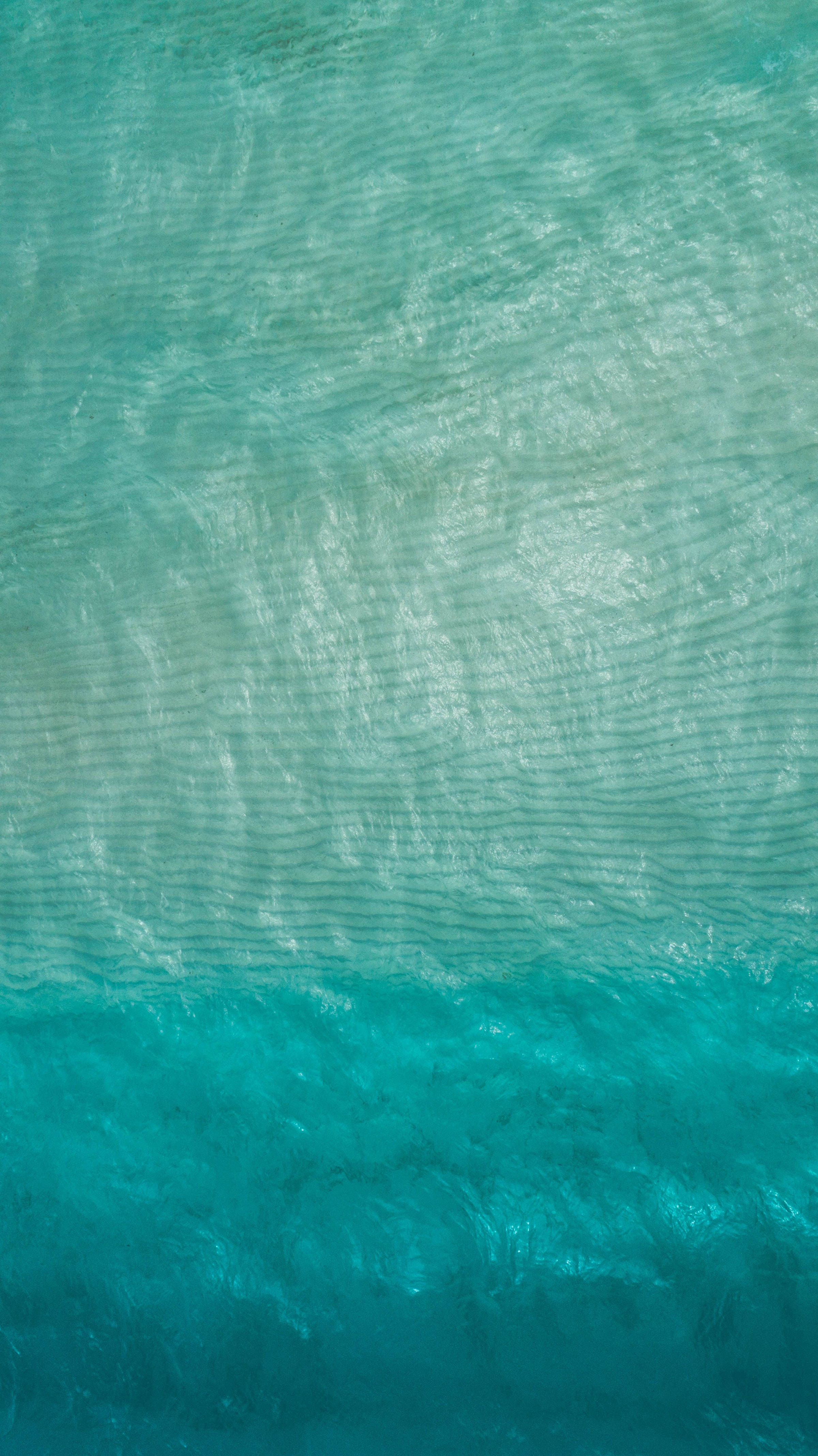 寧靜的海洋藍色水域 壁紙 — 從空中俯瞰綠松石色海浪，帶有輕柔漣漪，從淺藍到深藍的漸變。
