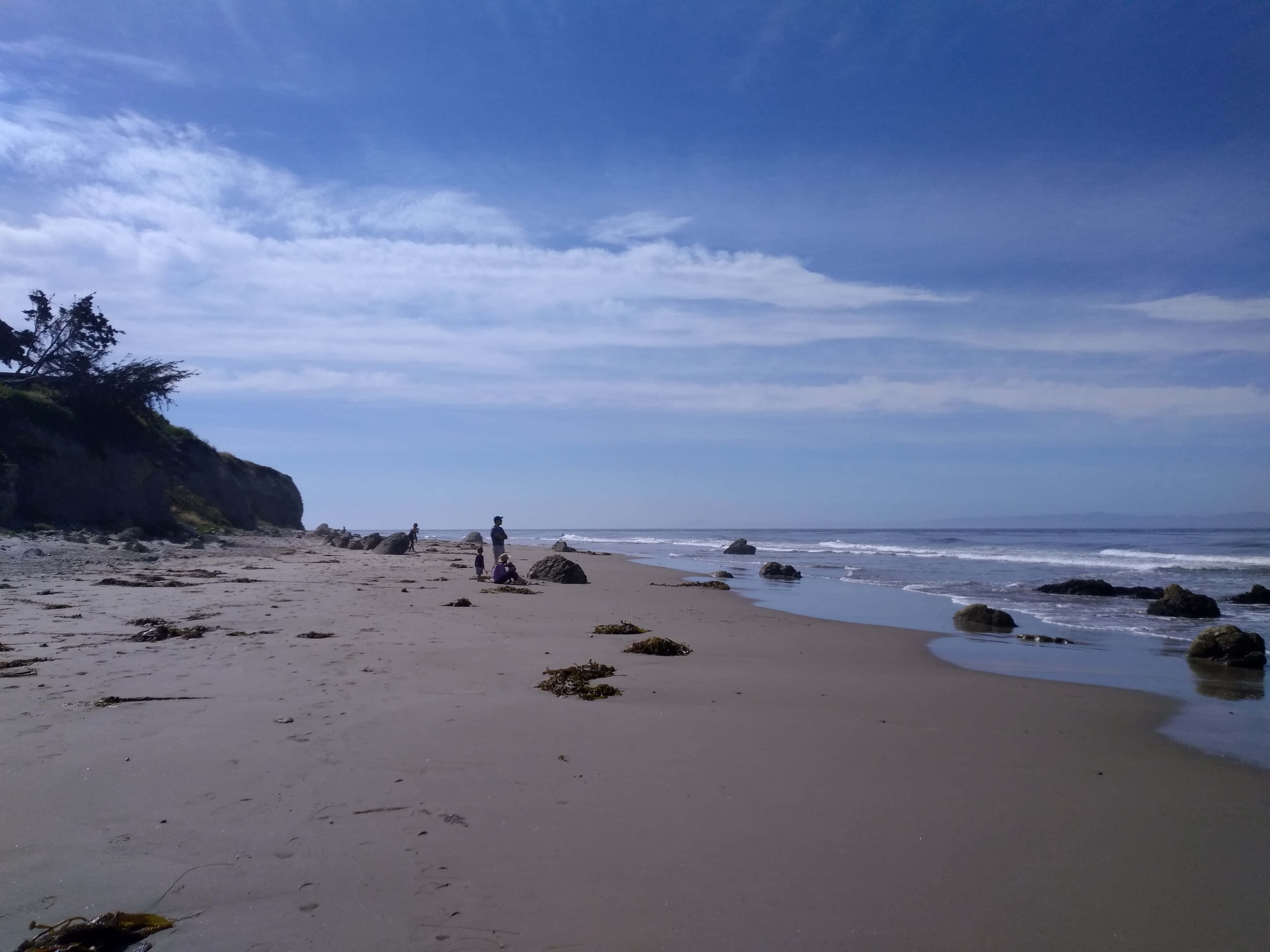 Beach Sand 桌布 壁紙 — 寧靜的海灘場景，溫柔的海浪輕拍海岸，廣闊的藍天點綴著縷縷白雲。