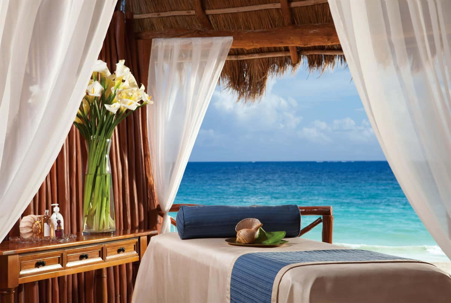Beach Daybed 桌布 壁紙 — 寧靜的海邊按摩亭，白色窗簾框住碧綠的海景，木桌上擺放黃色鮮花。