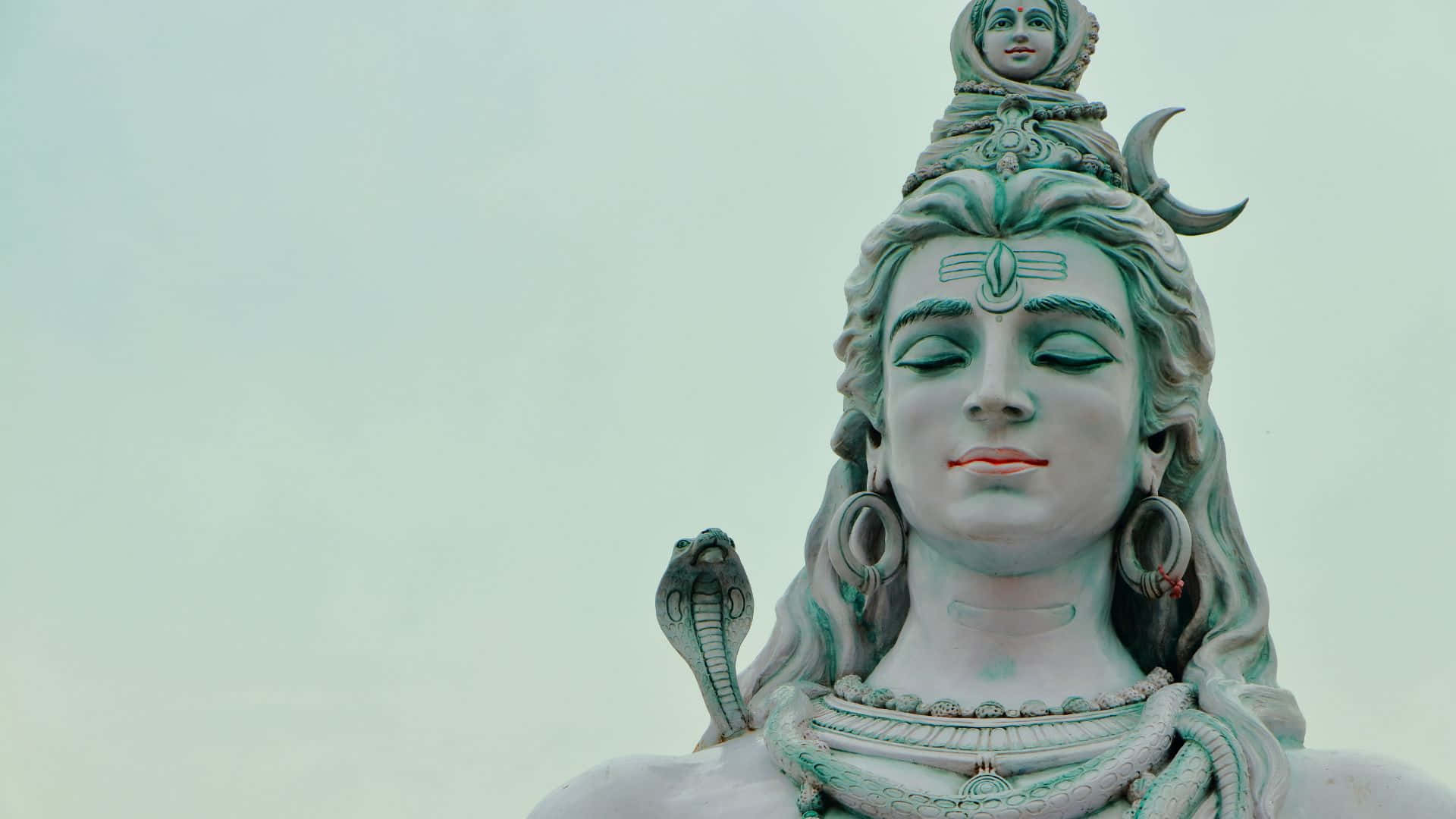 Shiva 桌布 壁紙 — 寧靜的濕婆神像特寫，閉著眼睛，新月和眼鏡蛇裝飾著頭部，背景是蒼白的天空。