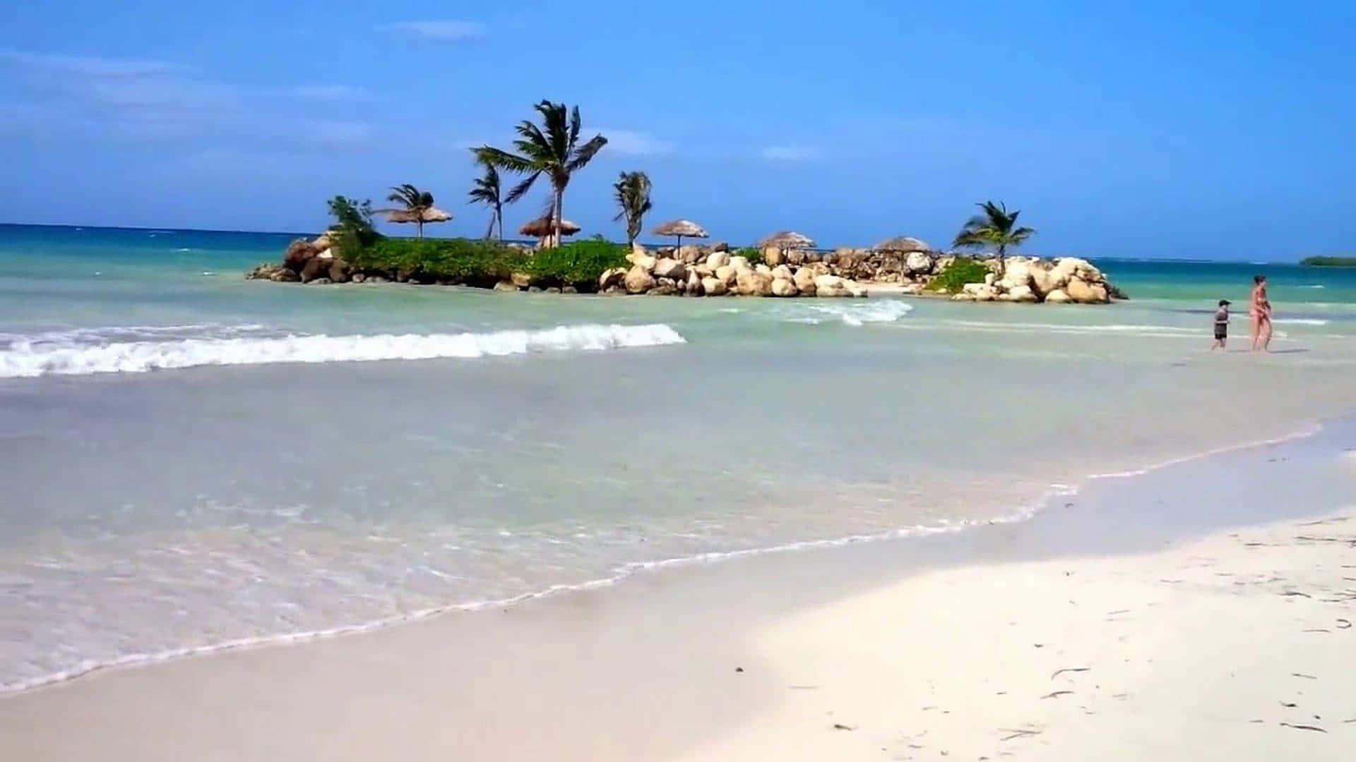 Jamaica 桌布 壁紙 — 寧靜的熱帶海灘，碧綠的海水，溫柔的海浪，以及一個點綴著棕櫚樹和茅草傘的小岩石島。