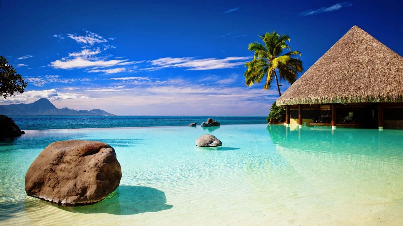 Beautiful Beach 桌布 壁紙 — 寧靜的熱帶無邊際泳池與碧綠海洋融為一體，上方是藍天白雲。