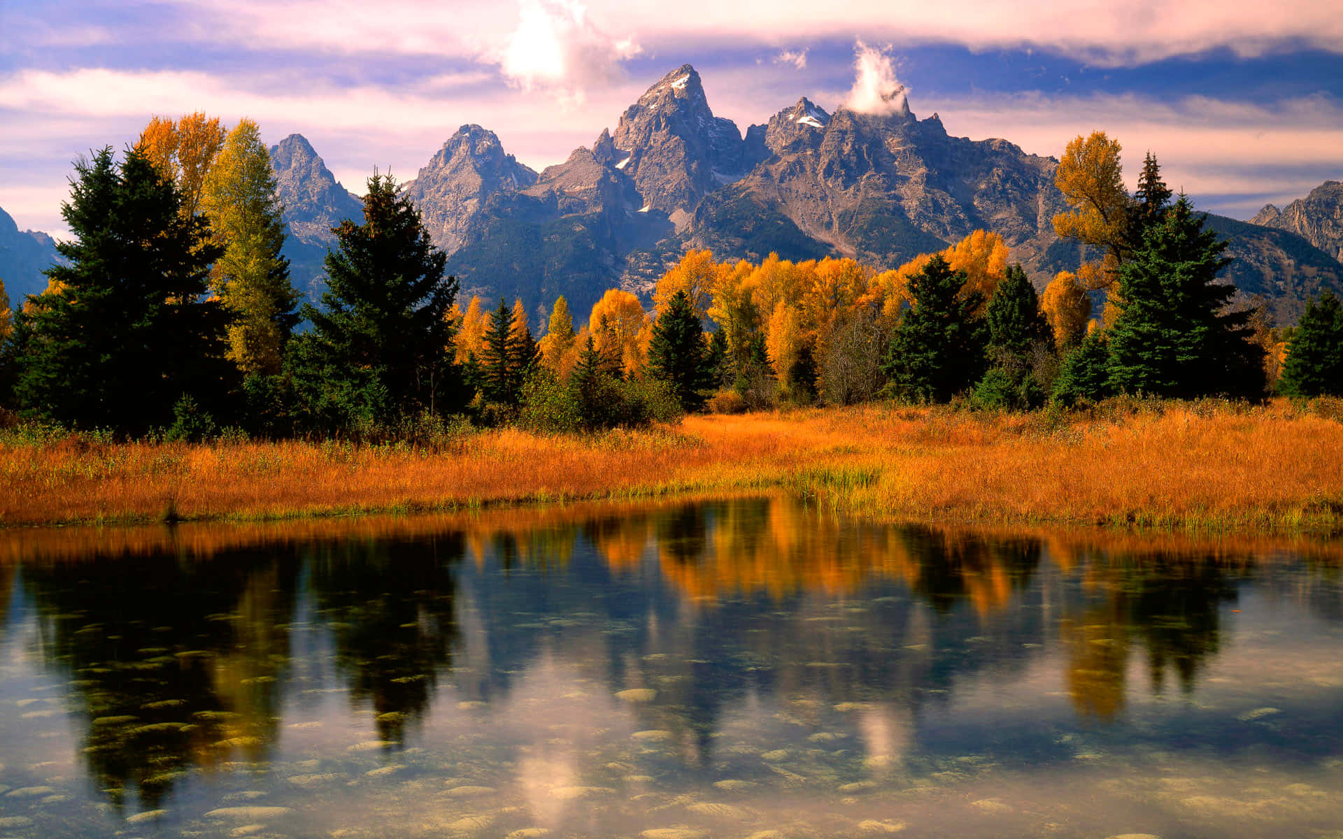 Fall Mountains 桌布 壁紙 — 寧靜的秋日景色，金色的草和色彩繽紛的樹木倒映在平靜的湖面上，背景是雄偉的雪山。