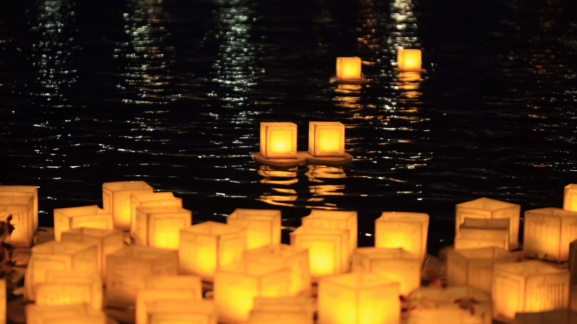 發光的燈籠在夜晚平靜的水面上漂浮，反射出金色光芒。