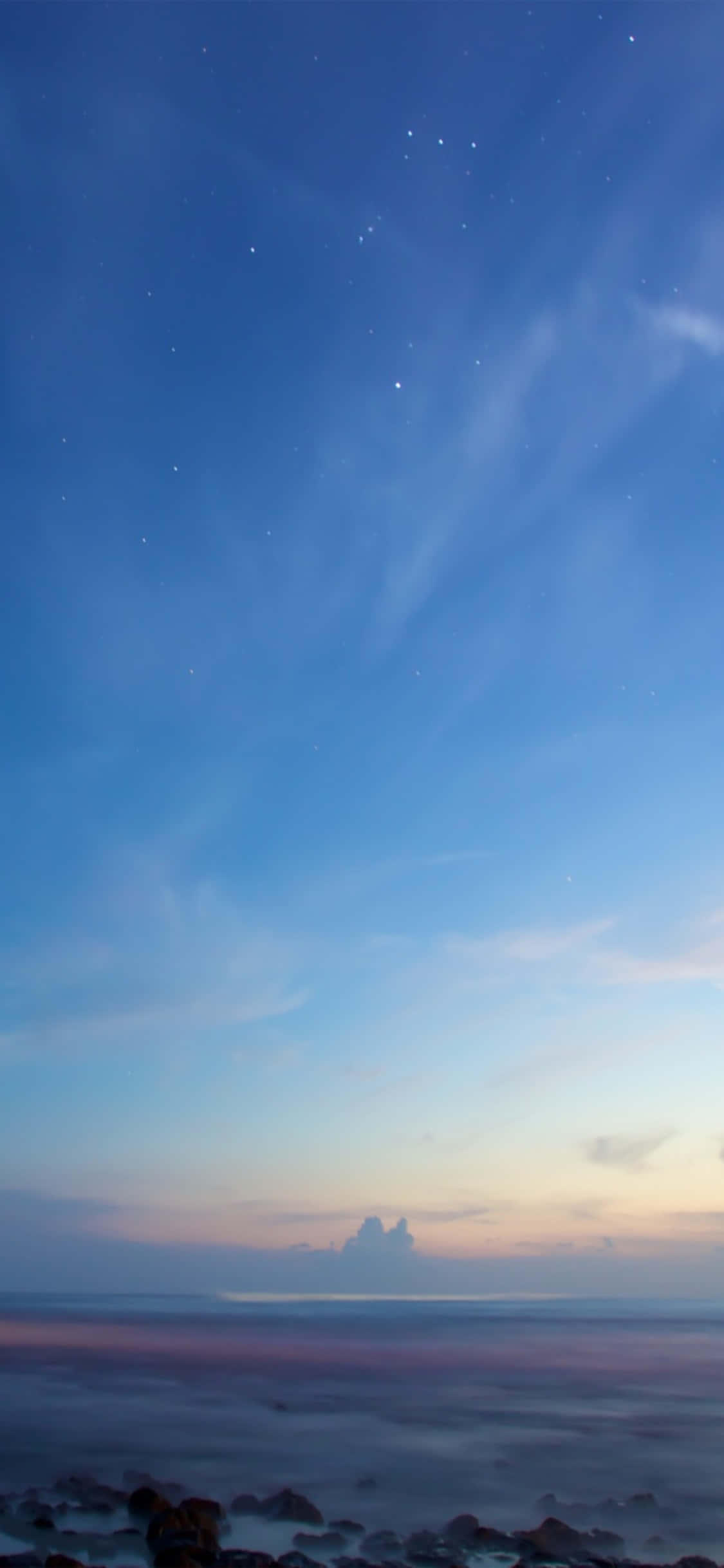 iPhone X 沙灘 桌布 壁紙 — 寧靜的黃昏海景，星星在漸變色的天空中浮現，映照在平靜的水面和深色岩石之上。
