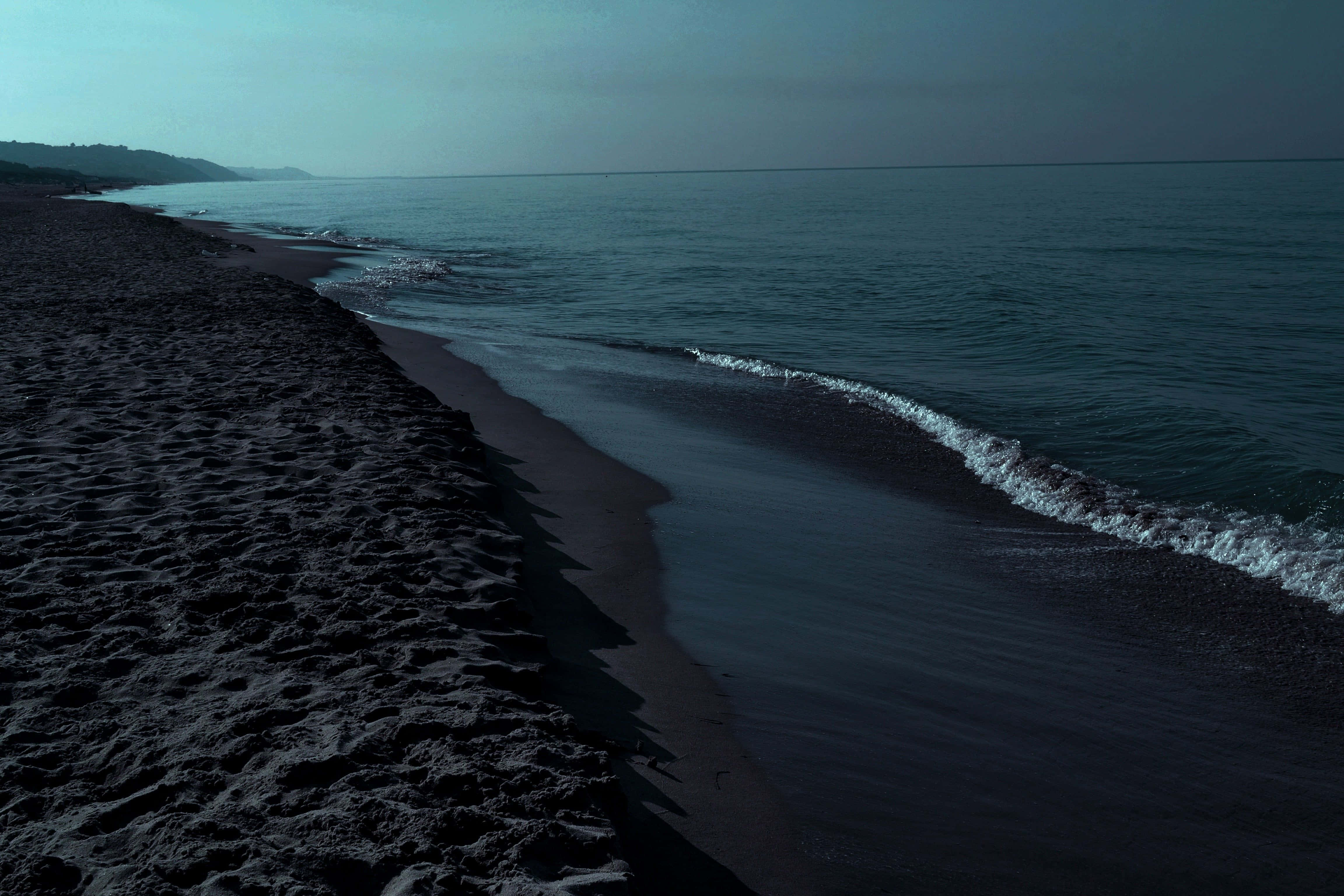 Black Sea 桌布 壁紙 — 寧靜的黃昏海灘，深色火山沙，柔和的海浪在暗淡的天空下拍打著海岸。